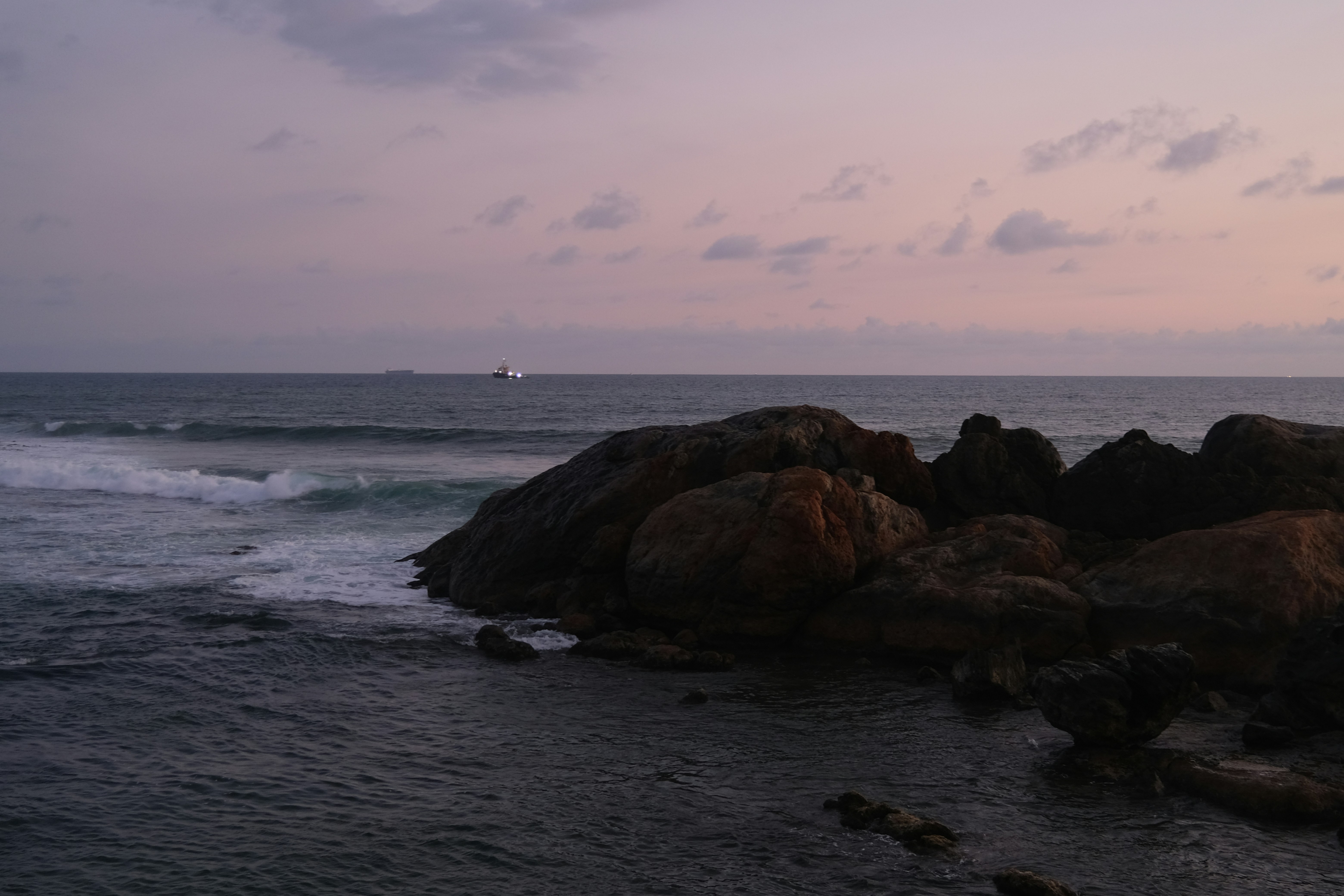 Pantai berbatu dengan ombak di bawah langit pastel