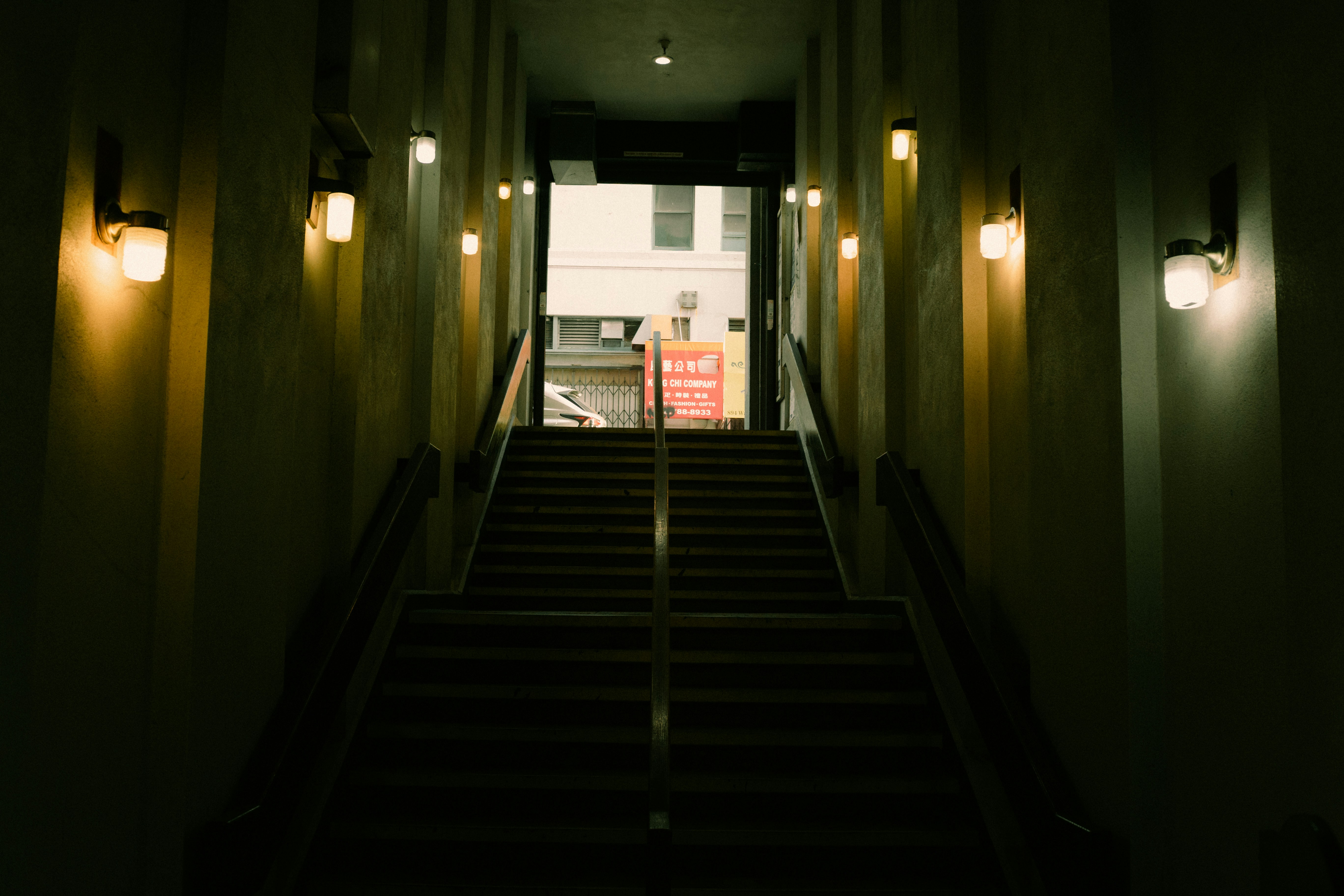 Dark staircase with wall sconces leading to bright exit.
