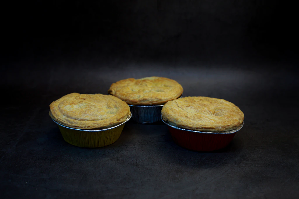 Three golden pies in foil trays on a dark background