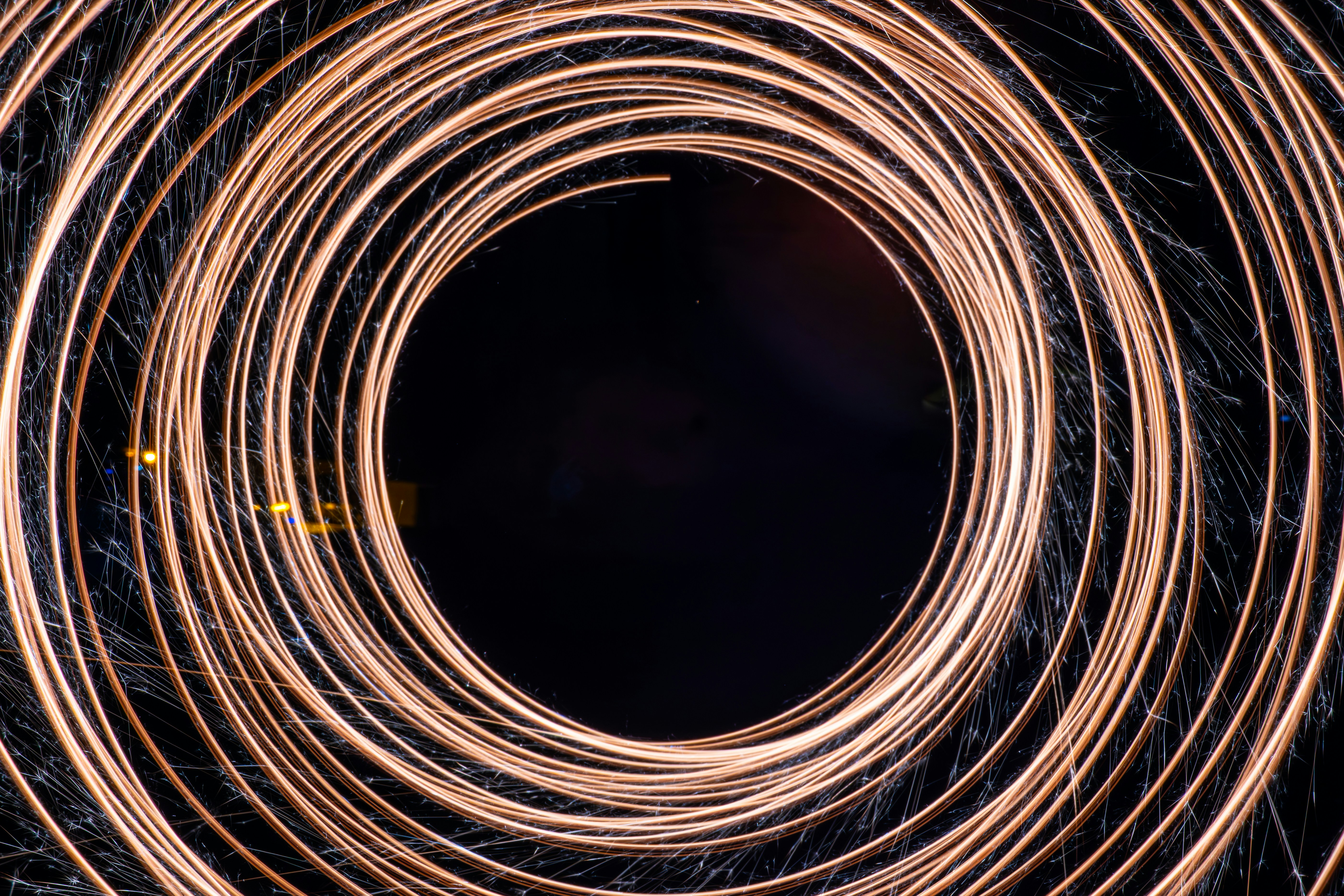 A long-exposure photograph capturing glowing circular light trails spiraling around a dark center, likely created with spinning a sparkler
