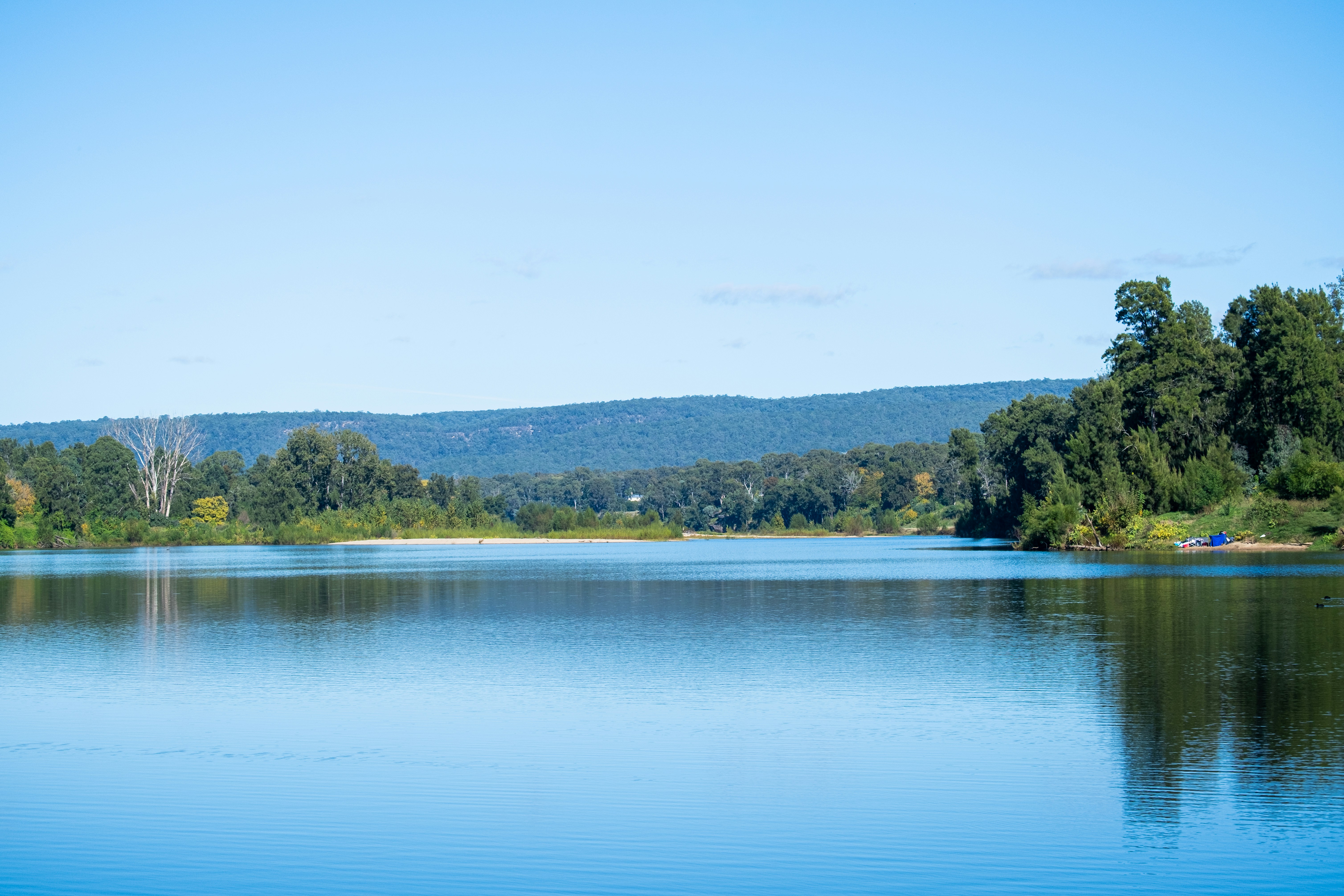 Lago azzurro e calmo circondato da alberi verdi rigogliosi e colline.