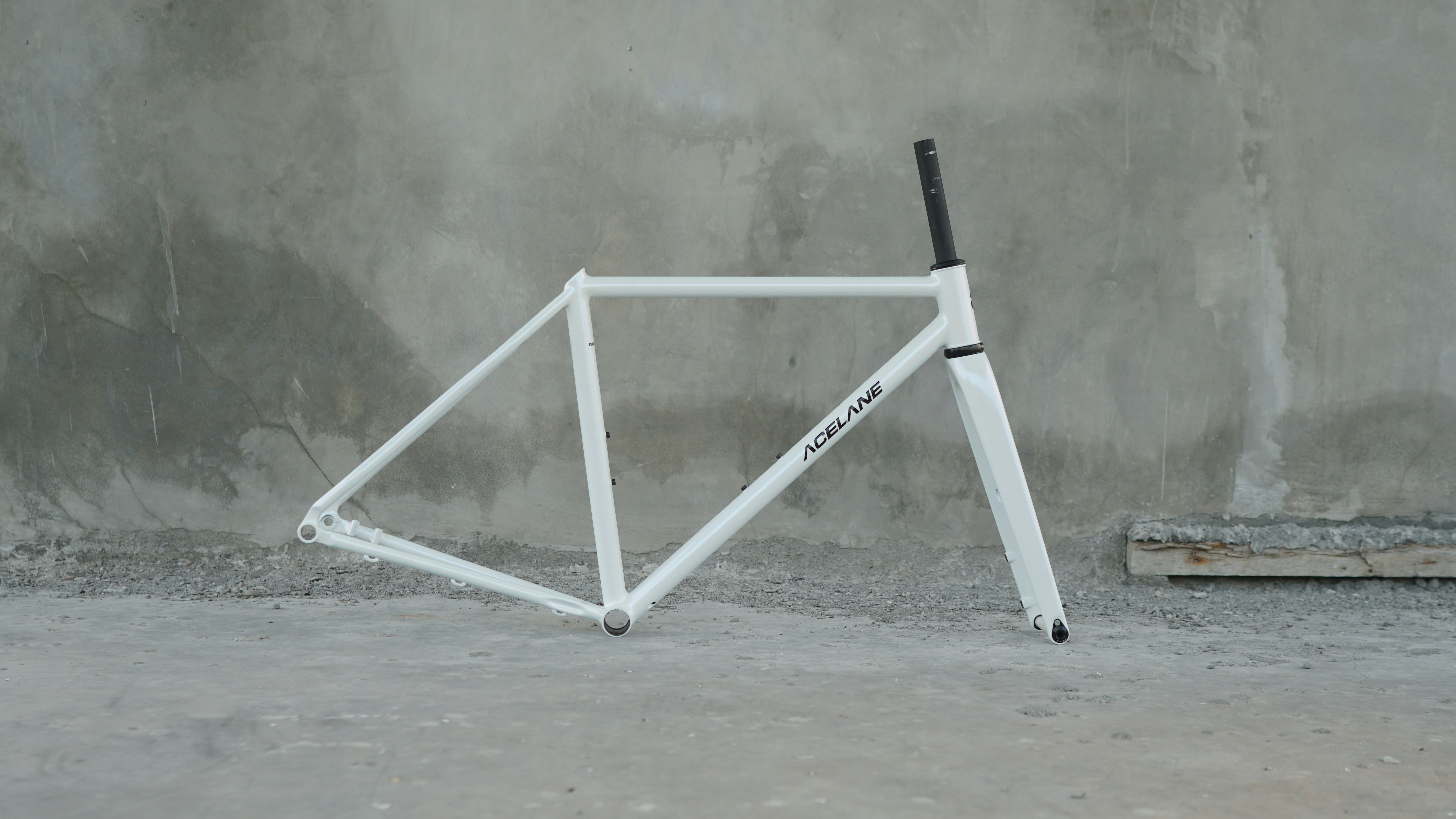 A white bicycle frame and fork against a concrete wall.