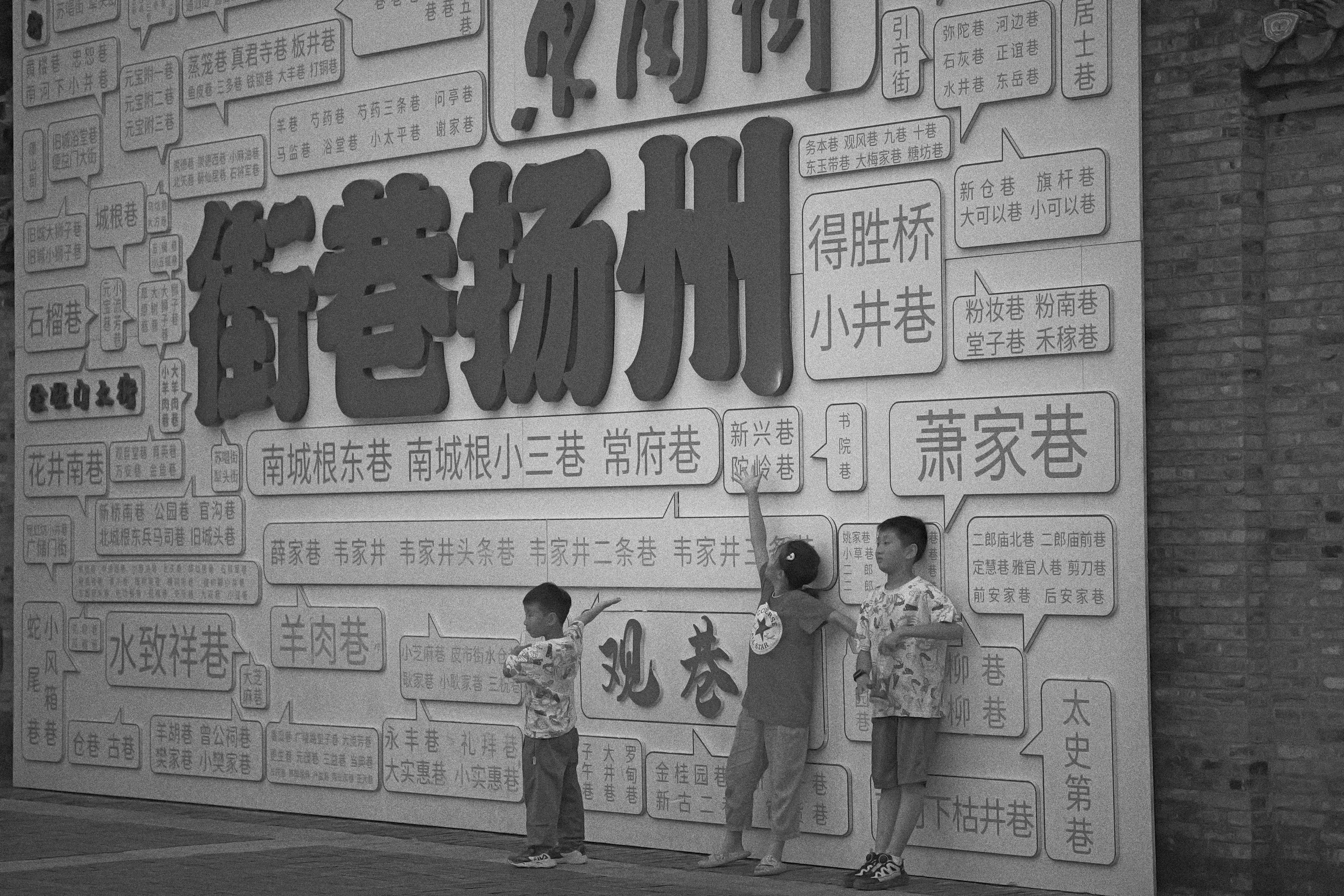 Three children pose in front of a large chinese mural