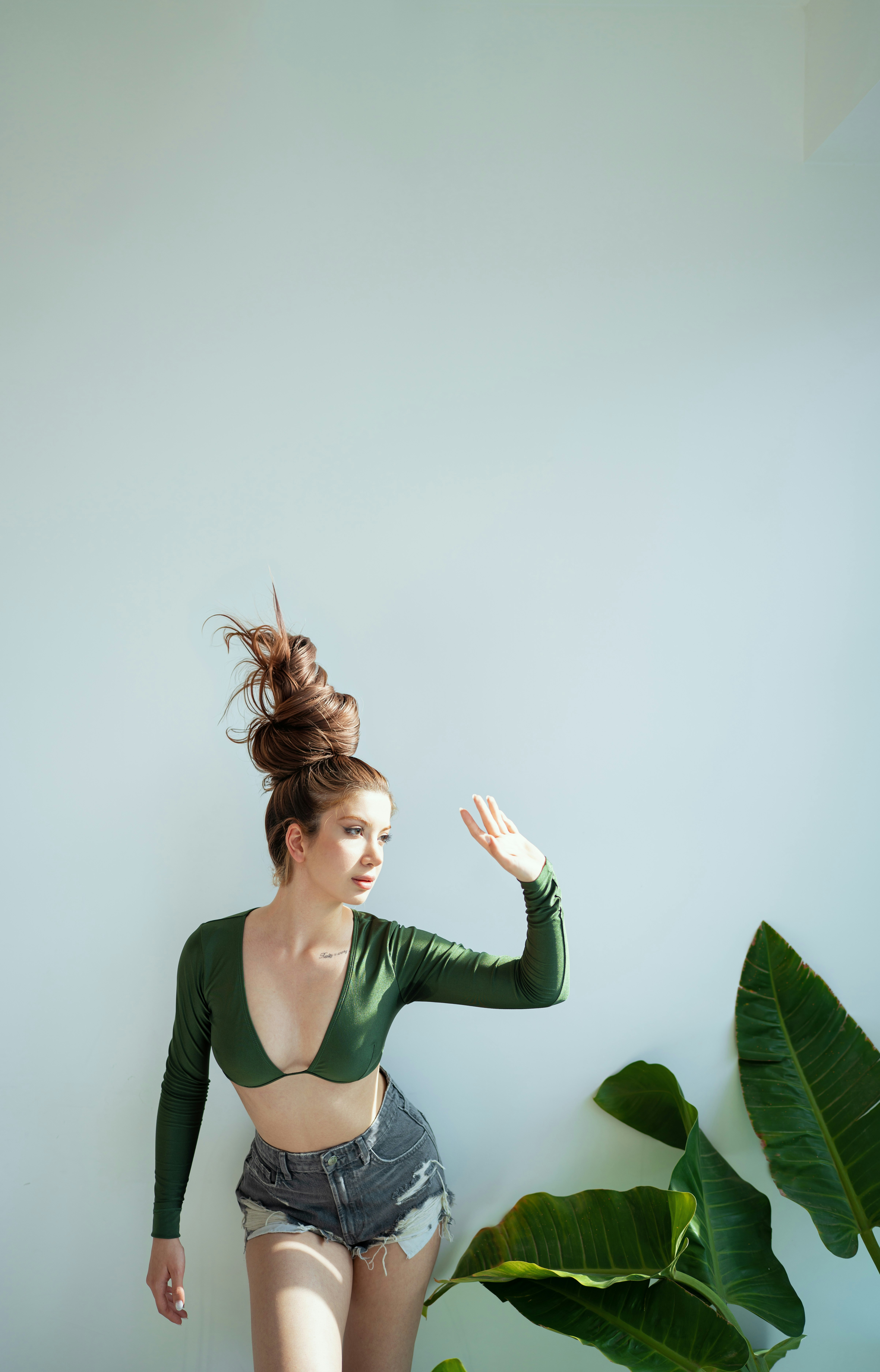 Woman with tall bun and green top poses by wall.
