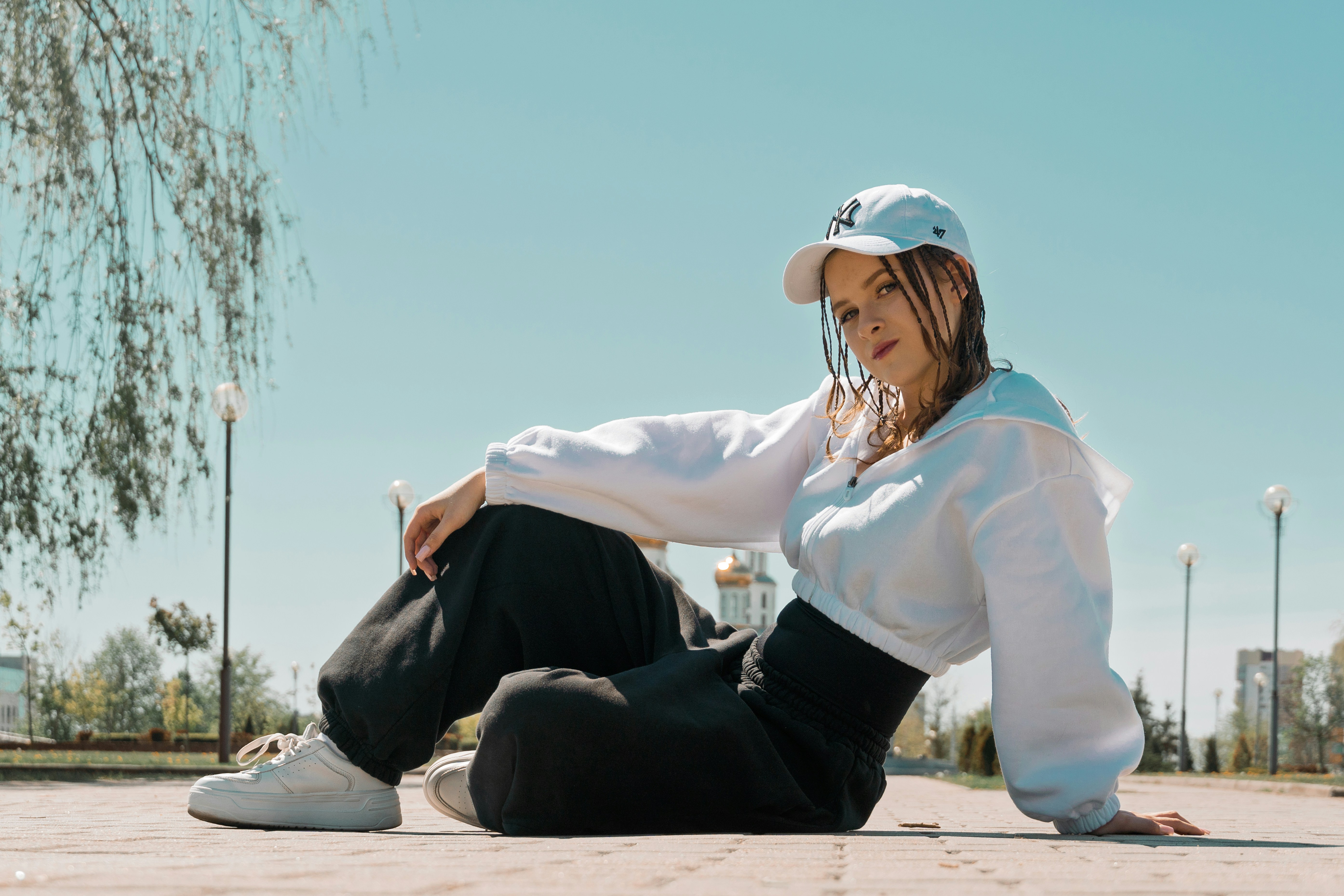 Young woman in white shirt and black pants sits outside.