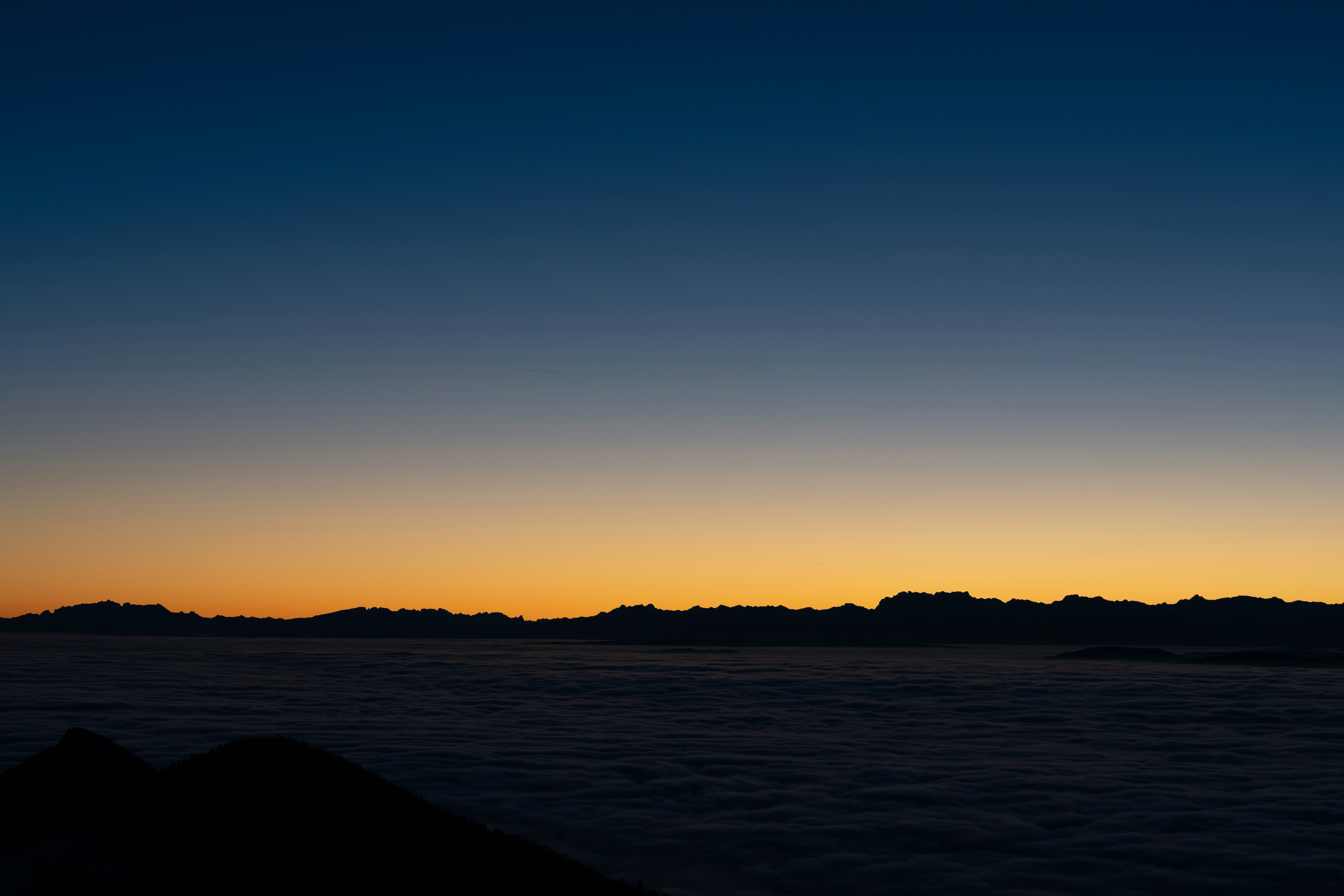 Mountain range silhouette at sunset above clouds