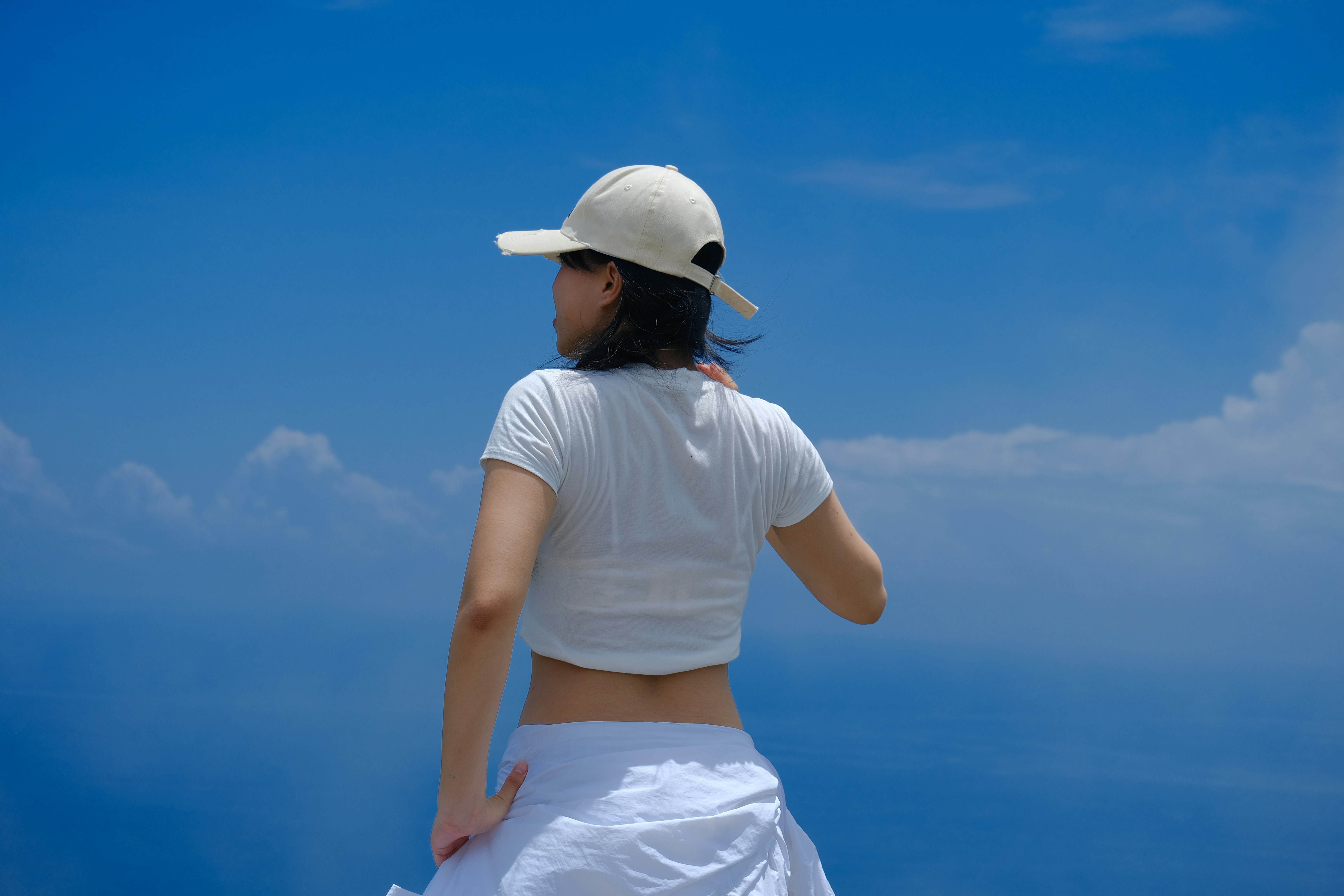 Mulher de camisa branca e boné contra o céu azul