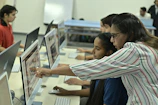 Teacher guiding students on computer in classroom.