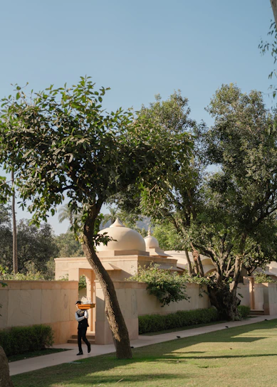 A person walks along a path near trees and buildings.
