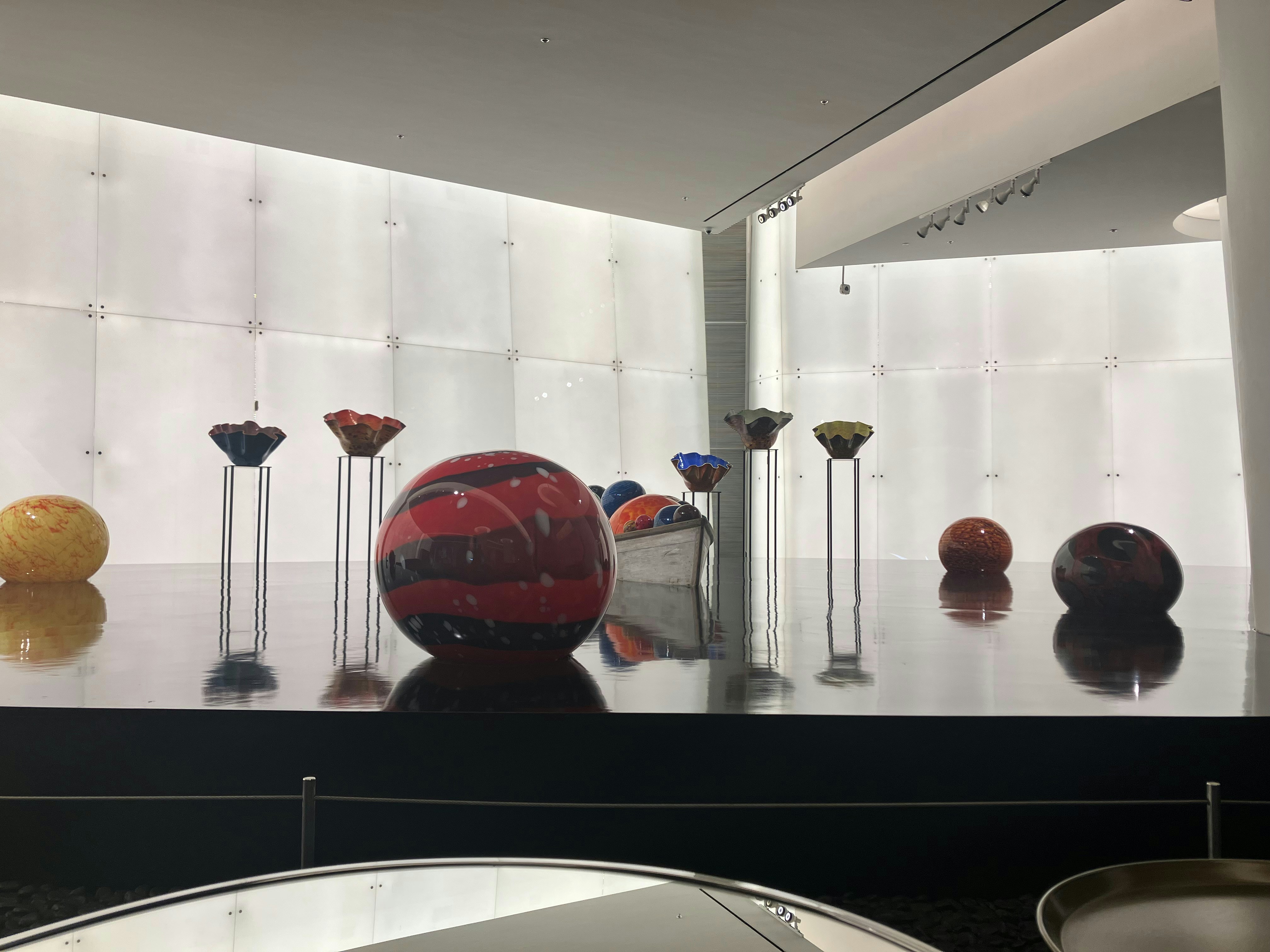 Bunte Glasskulpturen auf reflektierendem Boden in einer Galerie.