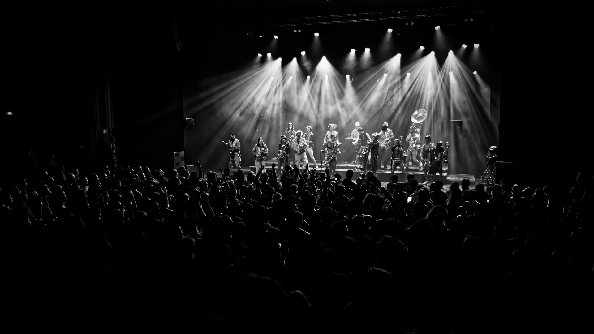 A band performs on stage with bright spotlights and audience