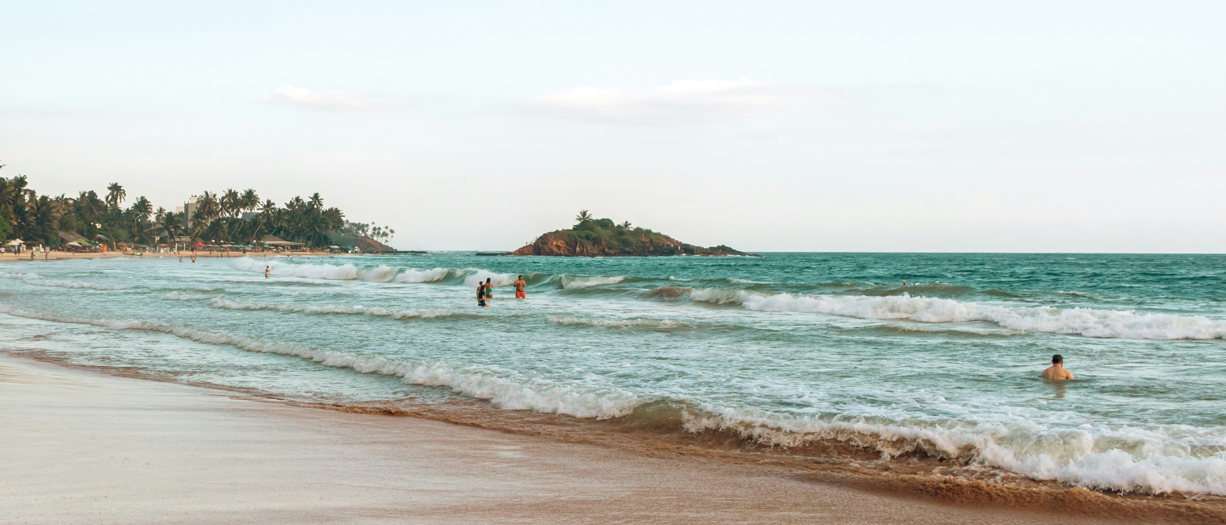 People swimming in the ocean near a tropical beach.