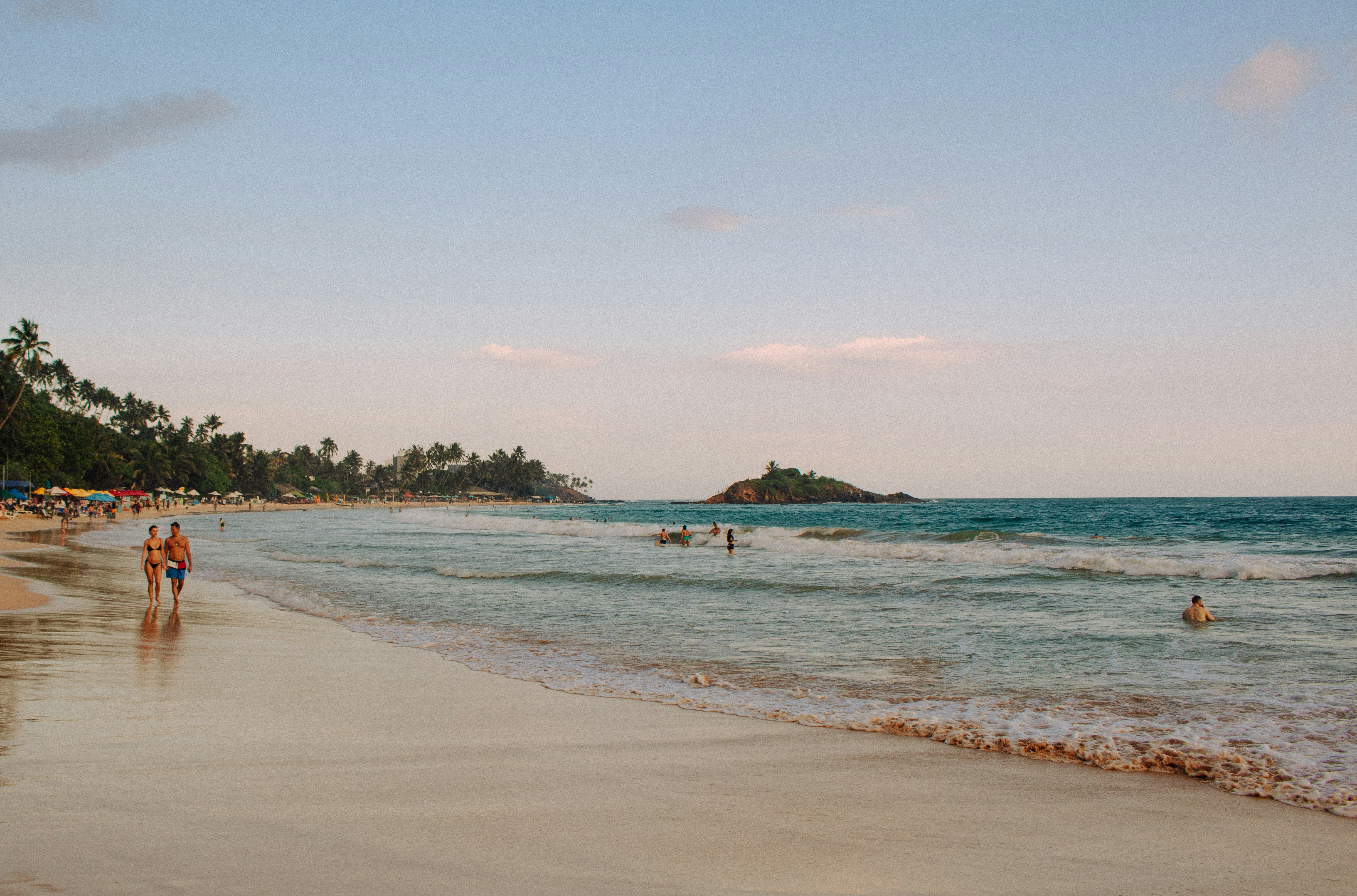 People walking on a sandy beach with ocean waves.