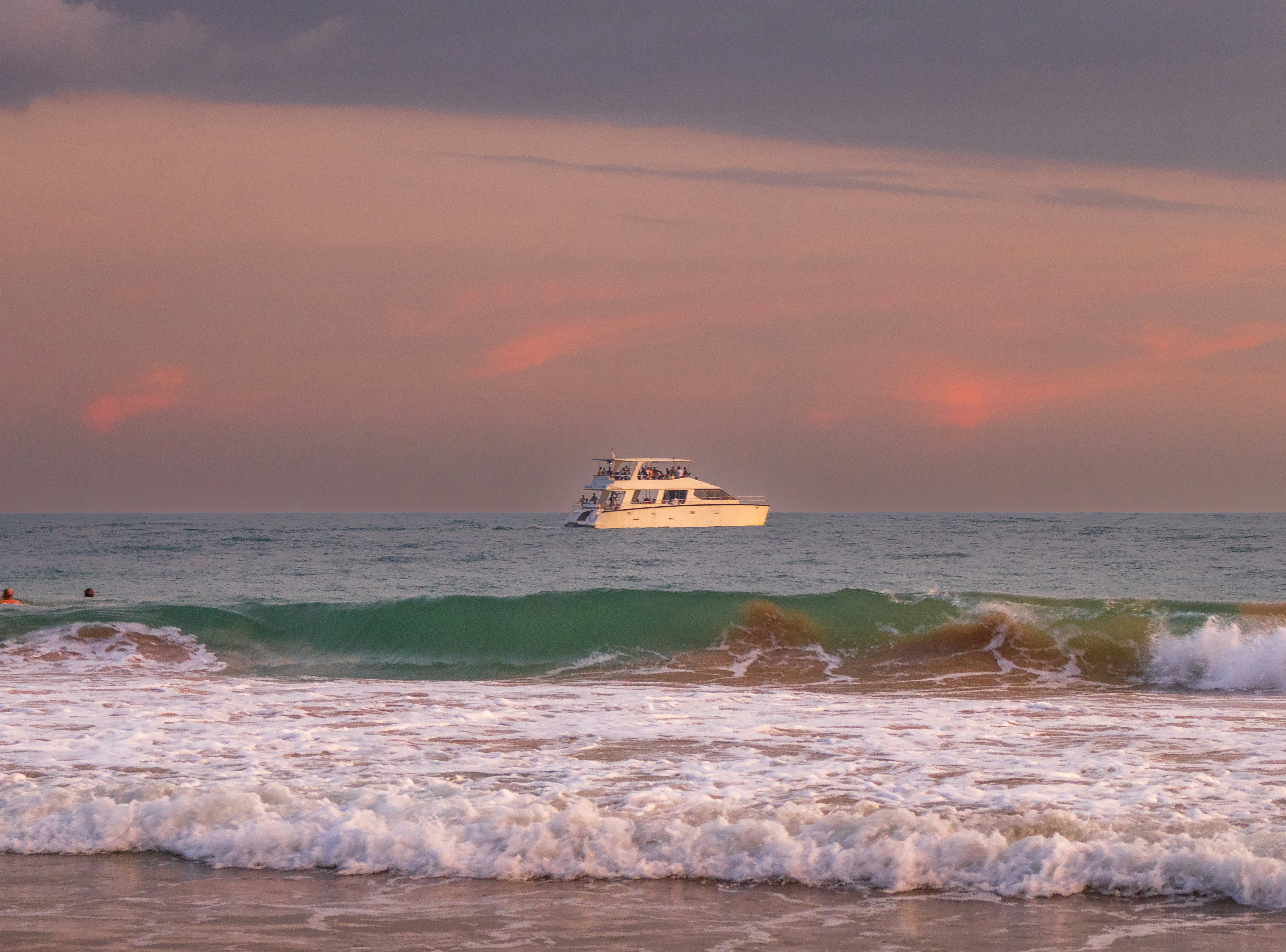A white boat sails on the ocean at sunset.