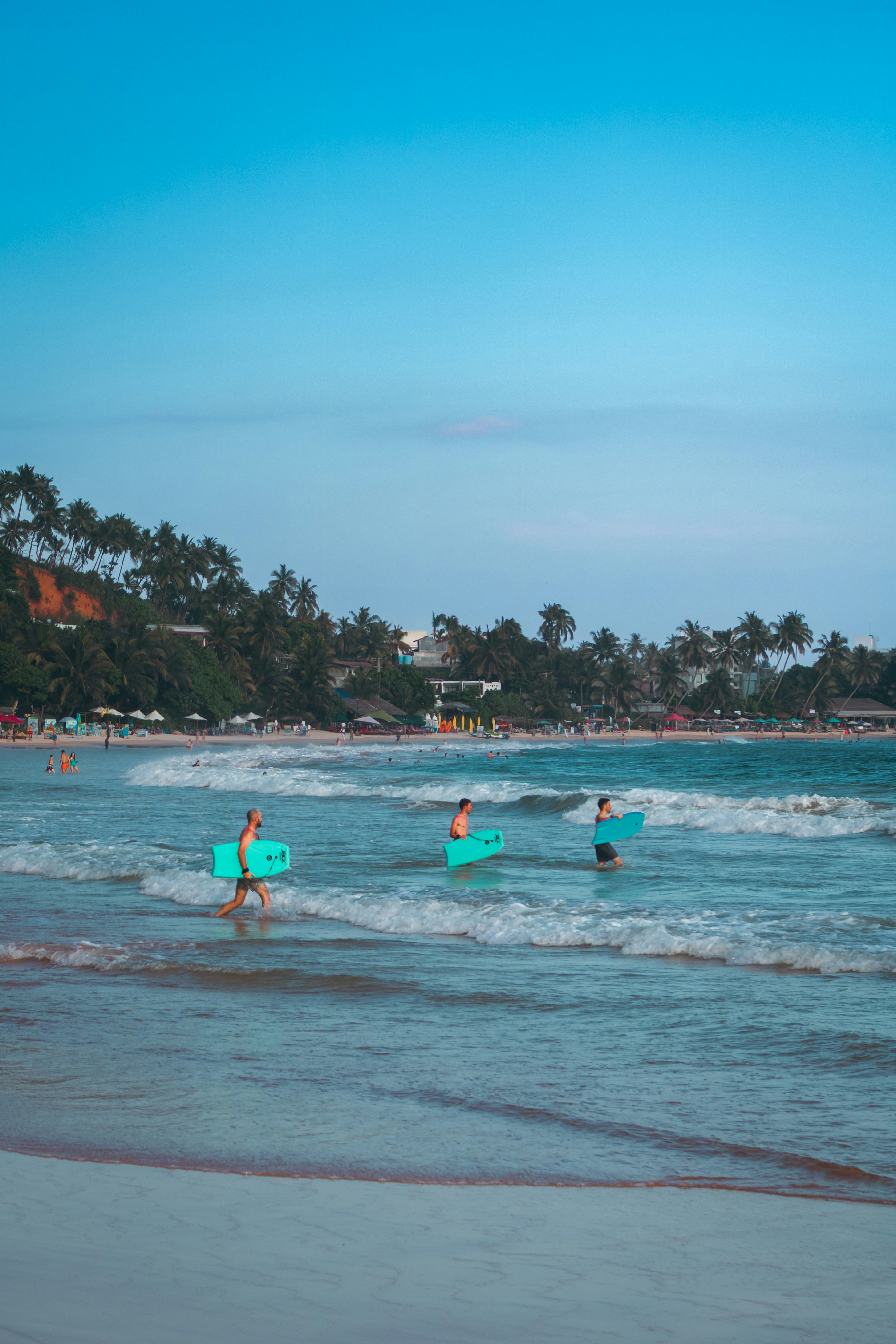 People carrying boogie boards walk into the ocean.