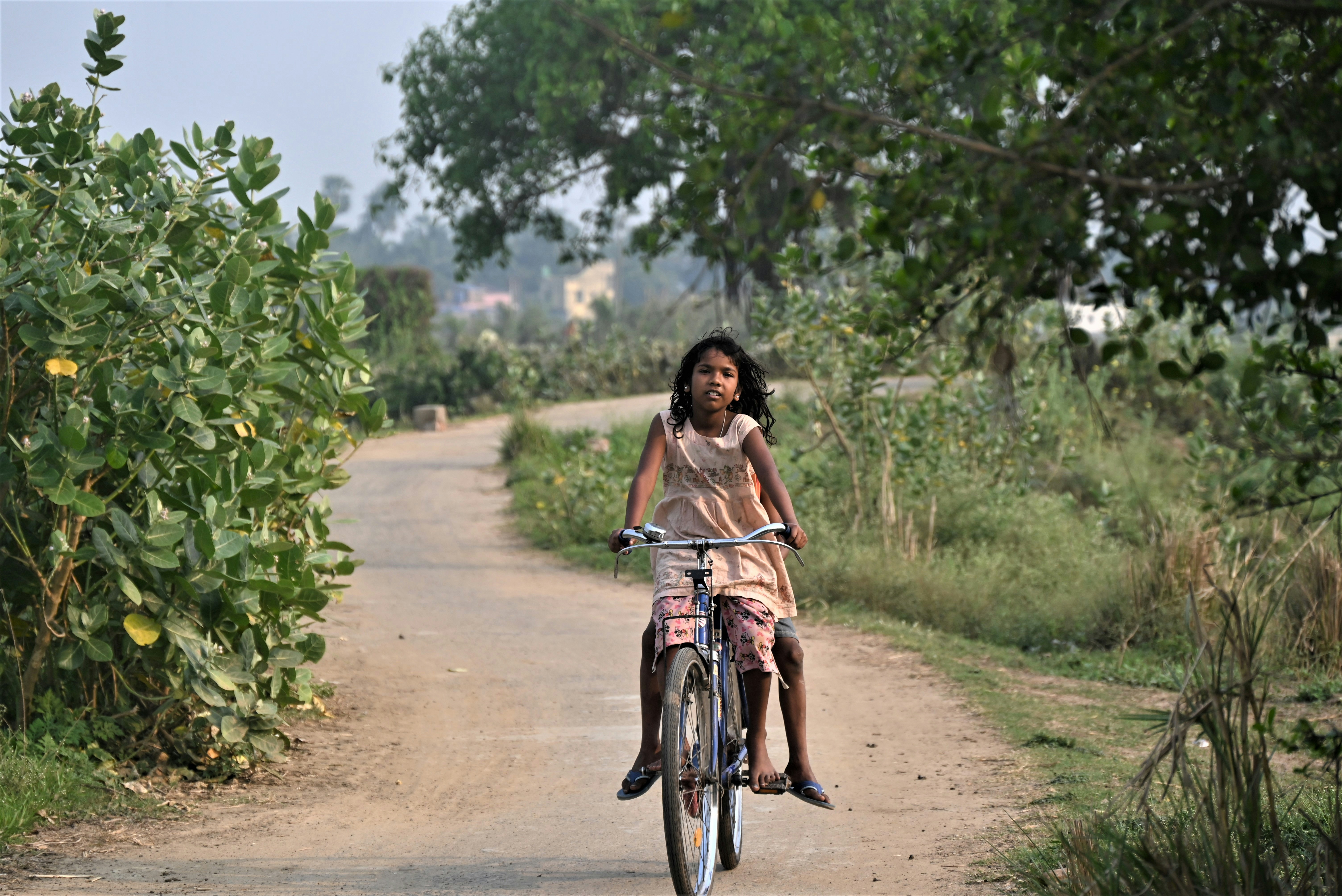 Uma jovem menina anda de bicicleta por uma estrada de terra.