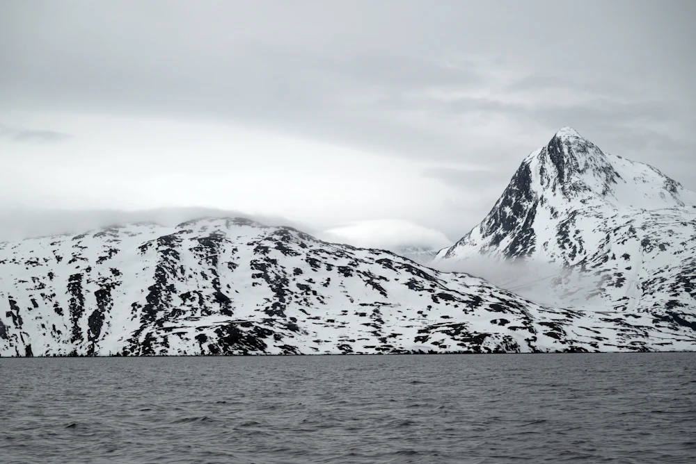 Snow-covered mountains rising straight out of the dark sea in East Greenland