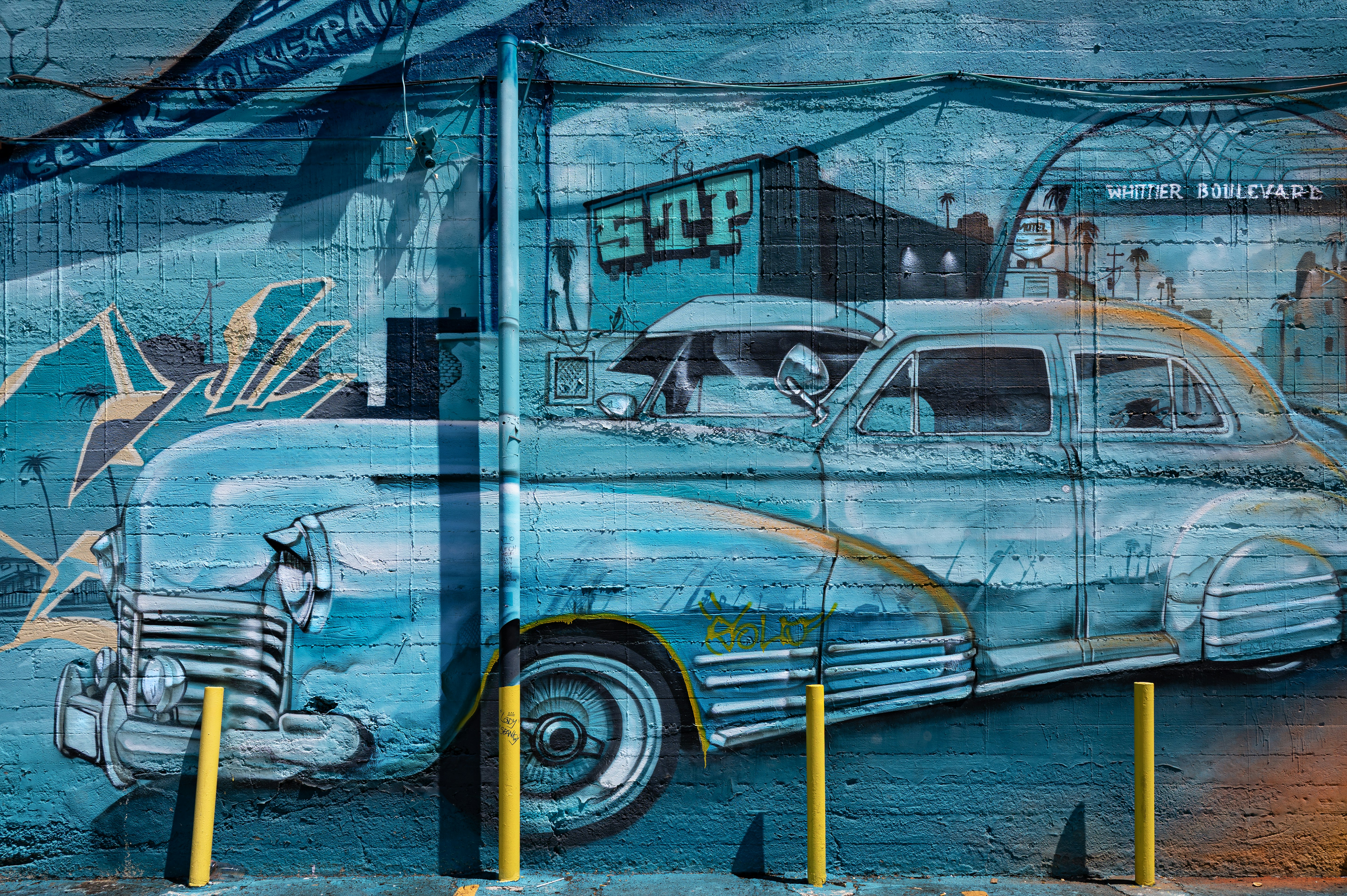 Vecchio murale di auto blu con pali gialli in primo piano.