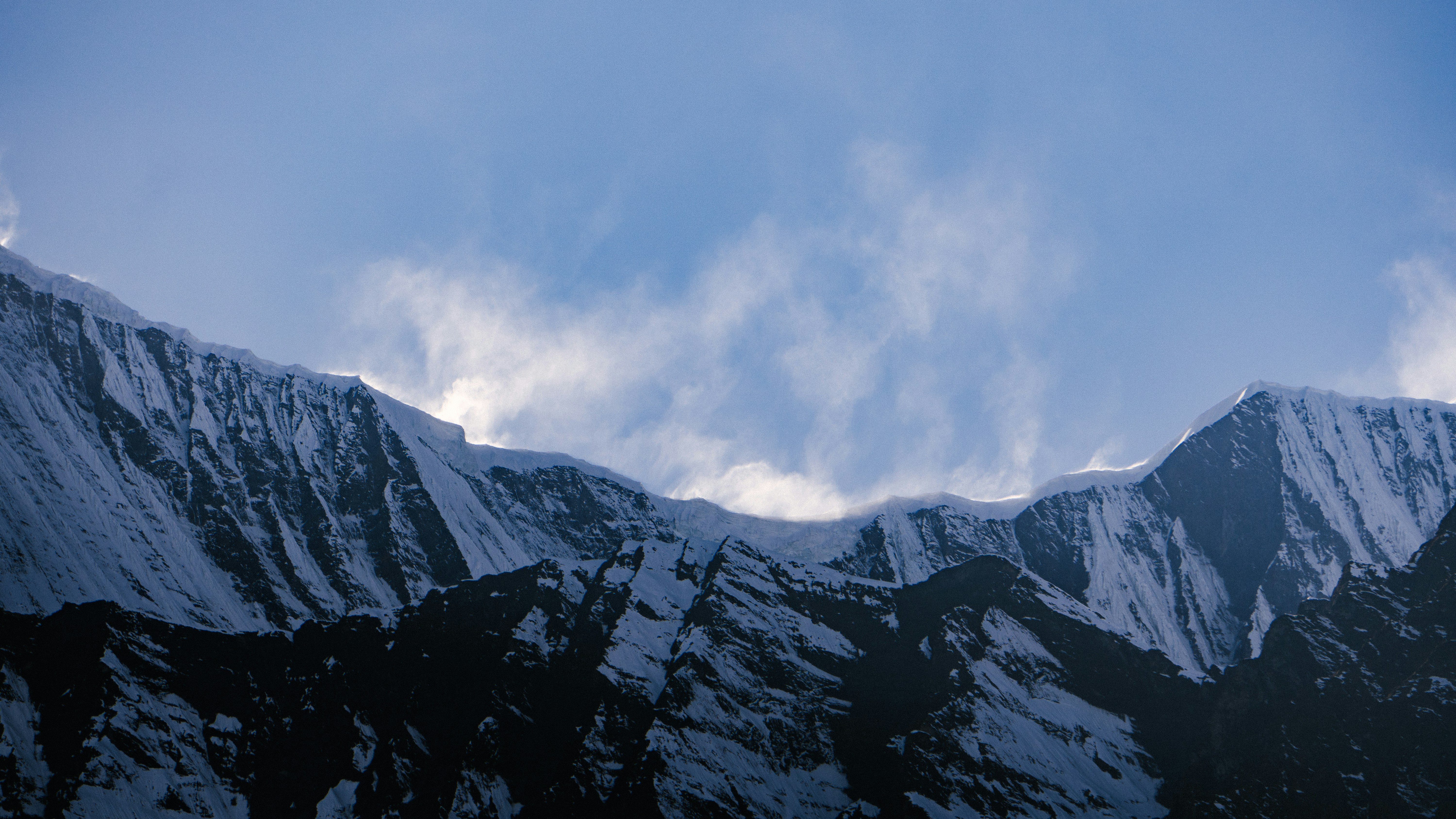 Montagne innevate sotto un cielo azzurro con nuvole sottili.