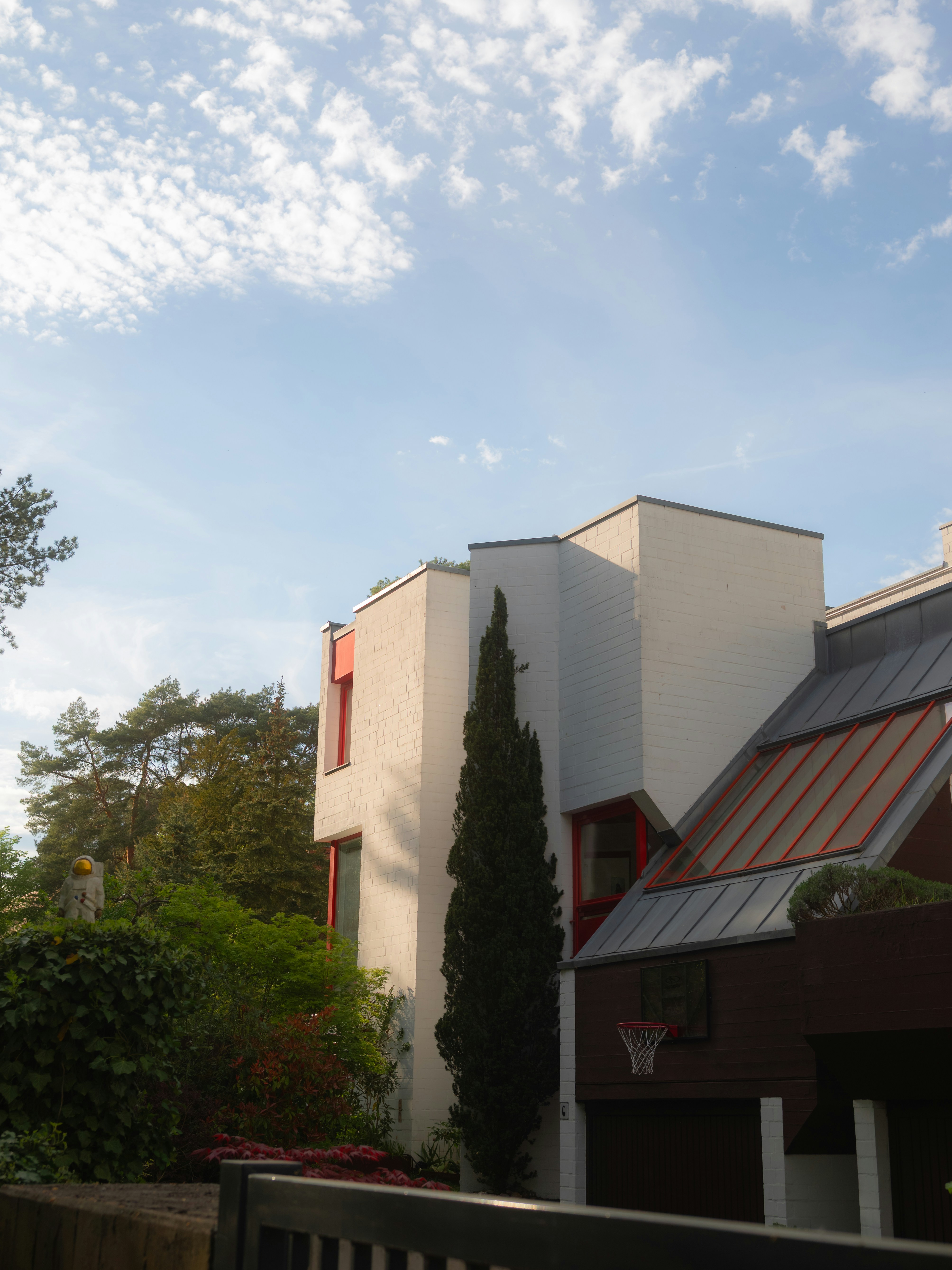 Modern house with white walls, red accents, and green trees.