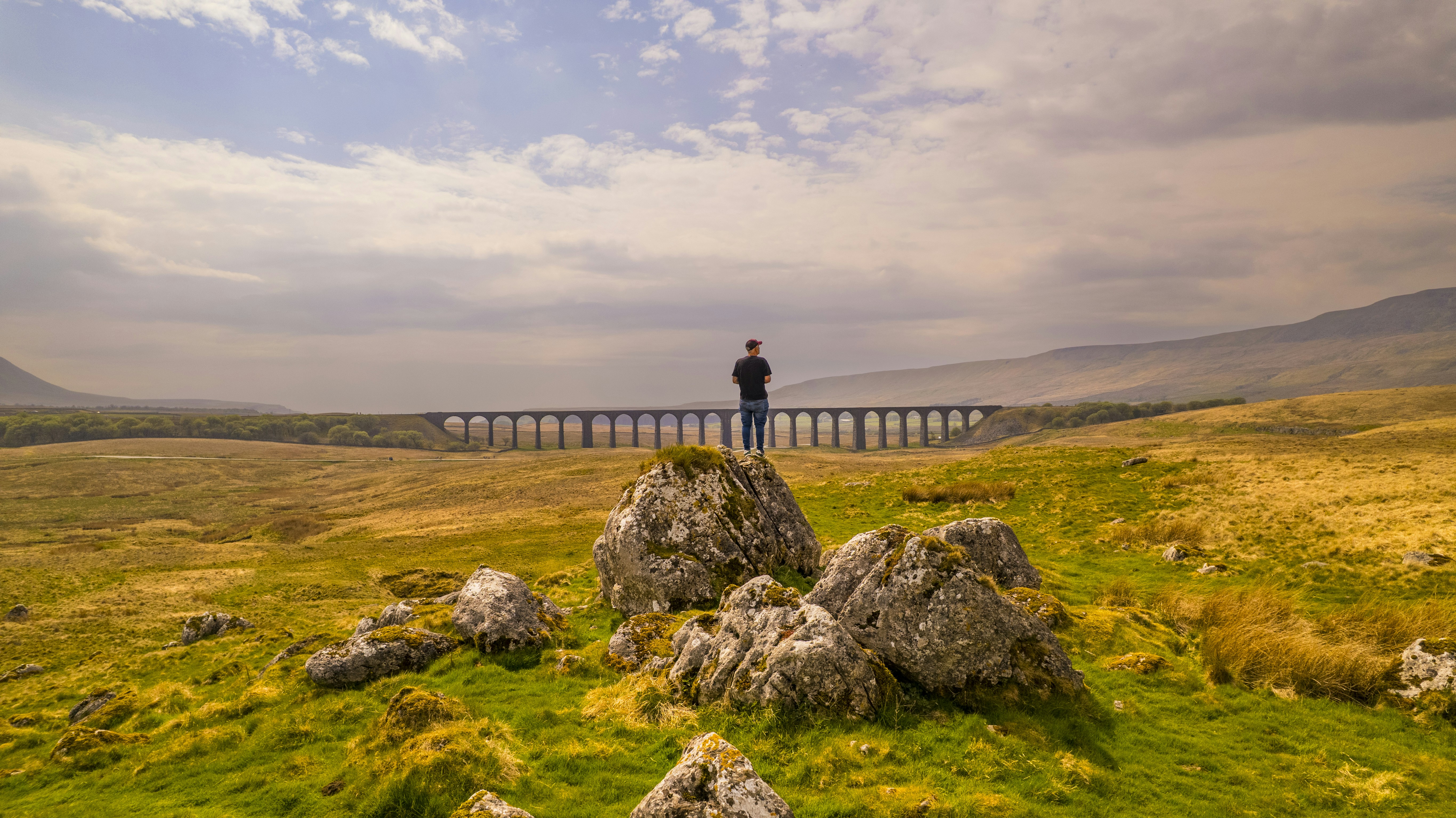 Man standing on rocks overlooking a distant viaduct