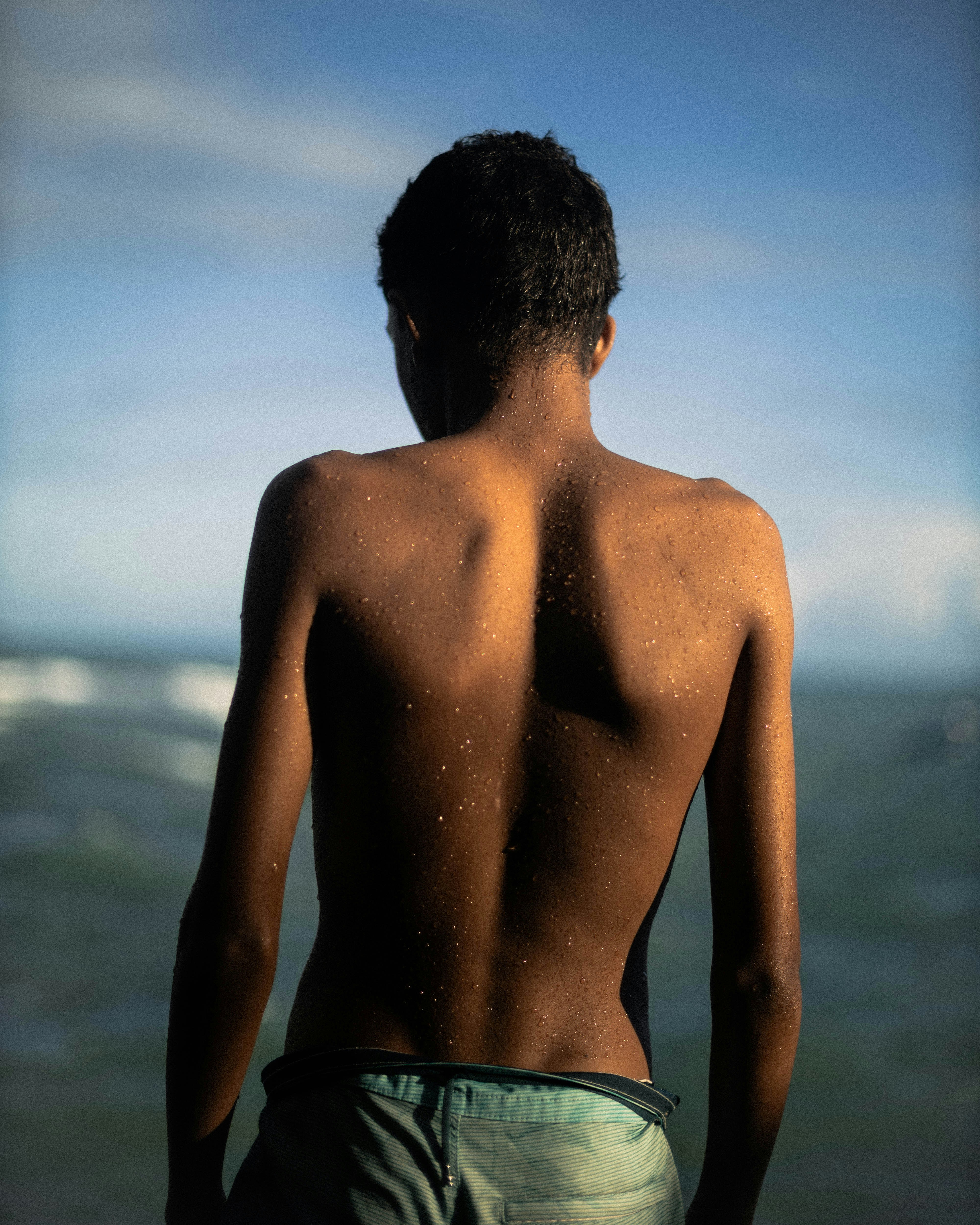 La espalda desnuda del joven mirando al océano bajo un cielo azul.