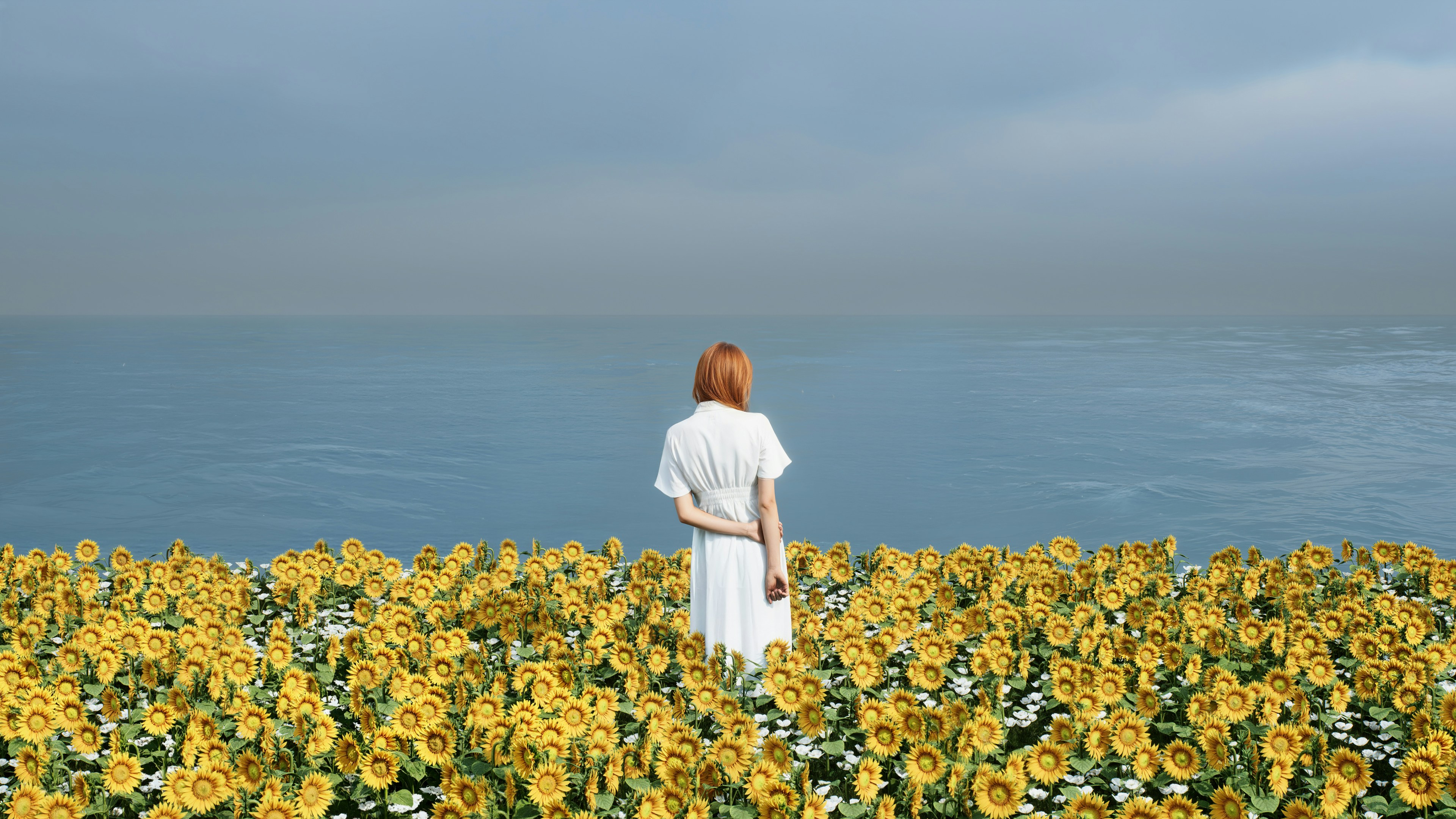Woman in white dress stands in sunflower field by sea