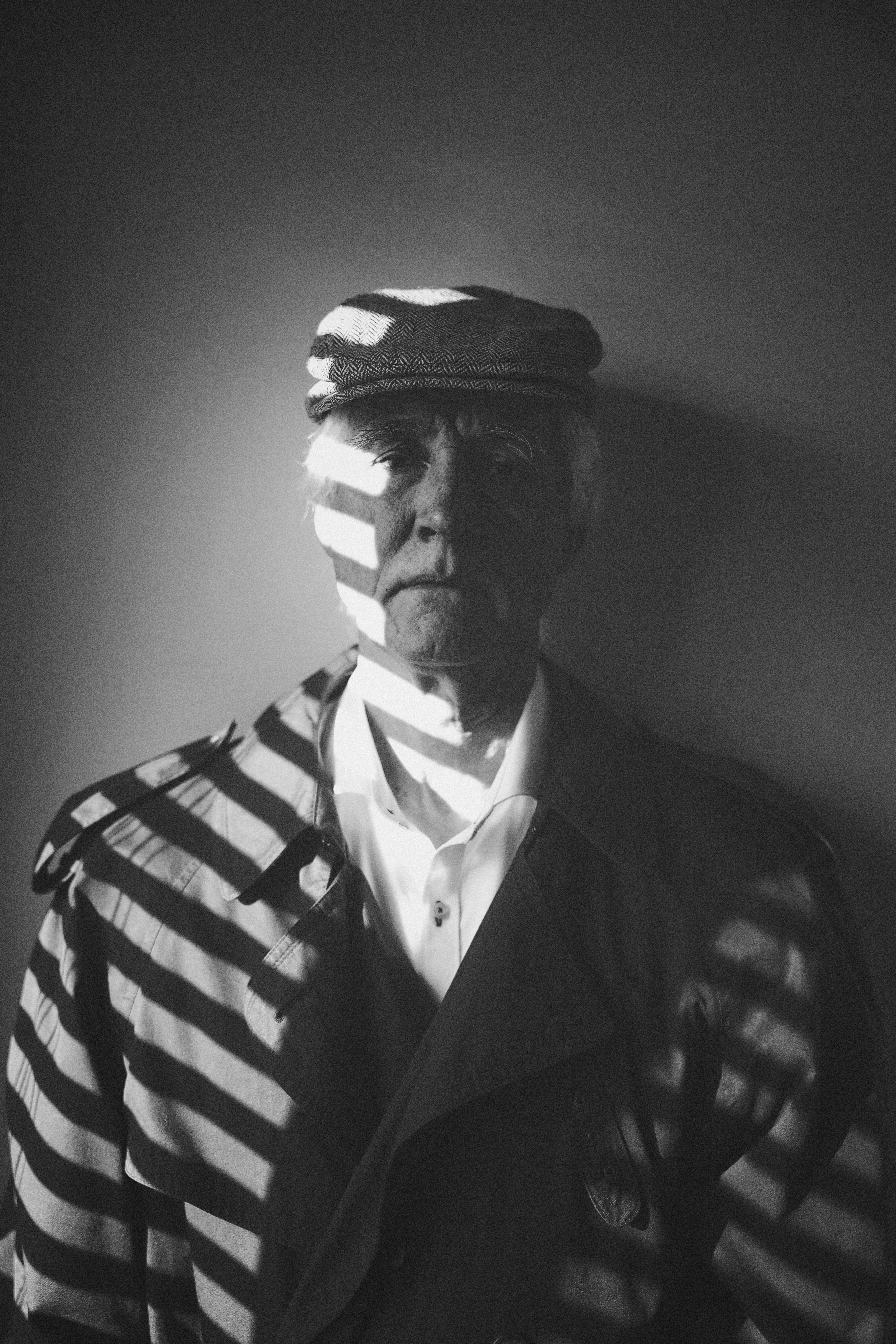 Man wearing a hat and trench coat with striped shadows.