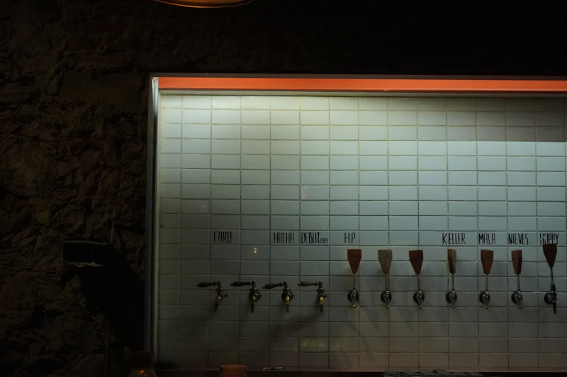 A row of labeled beer taps mounted on a tiled bar wall