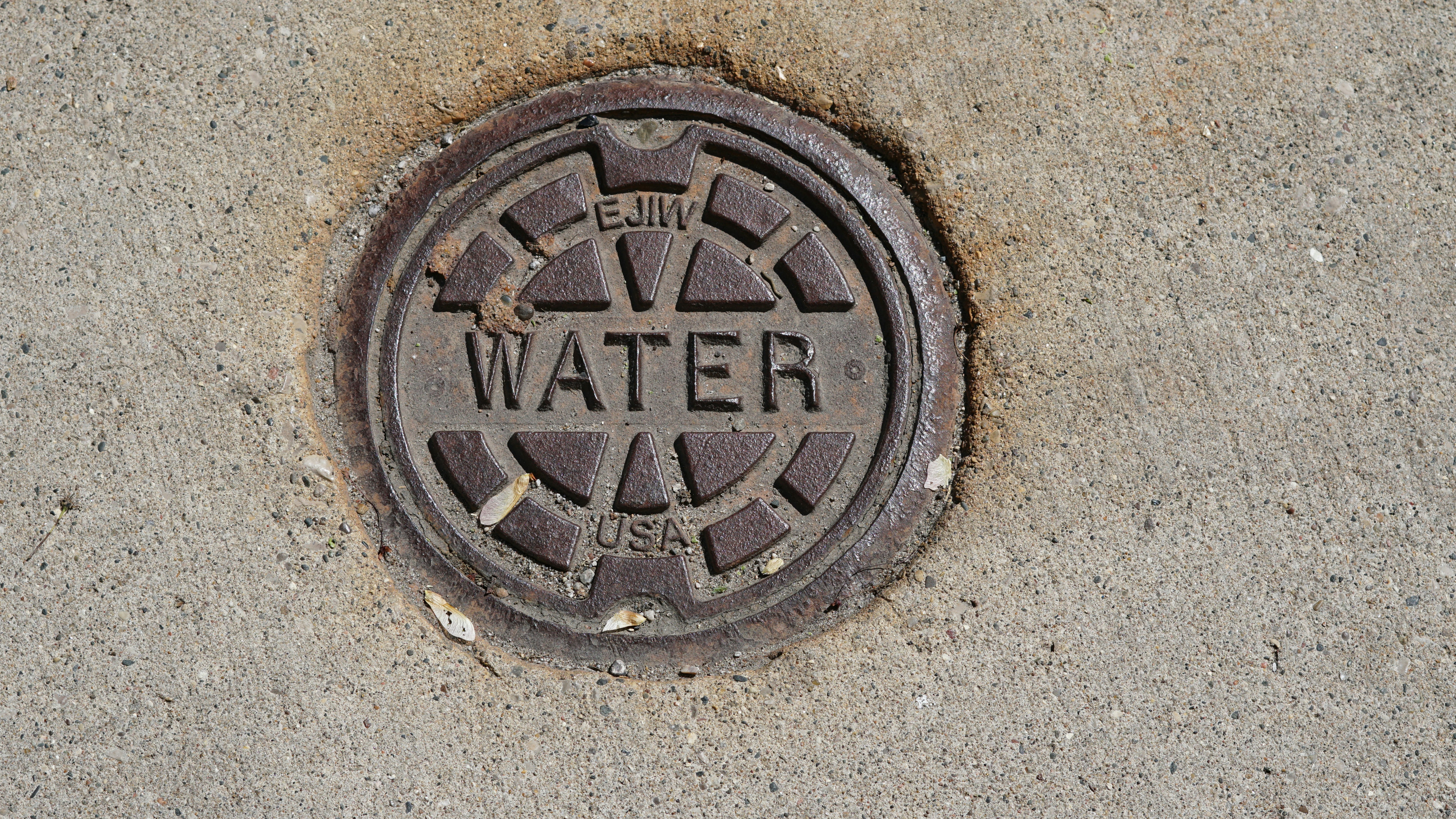 A circular metal water meter cover embedded in concrete.