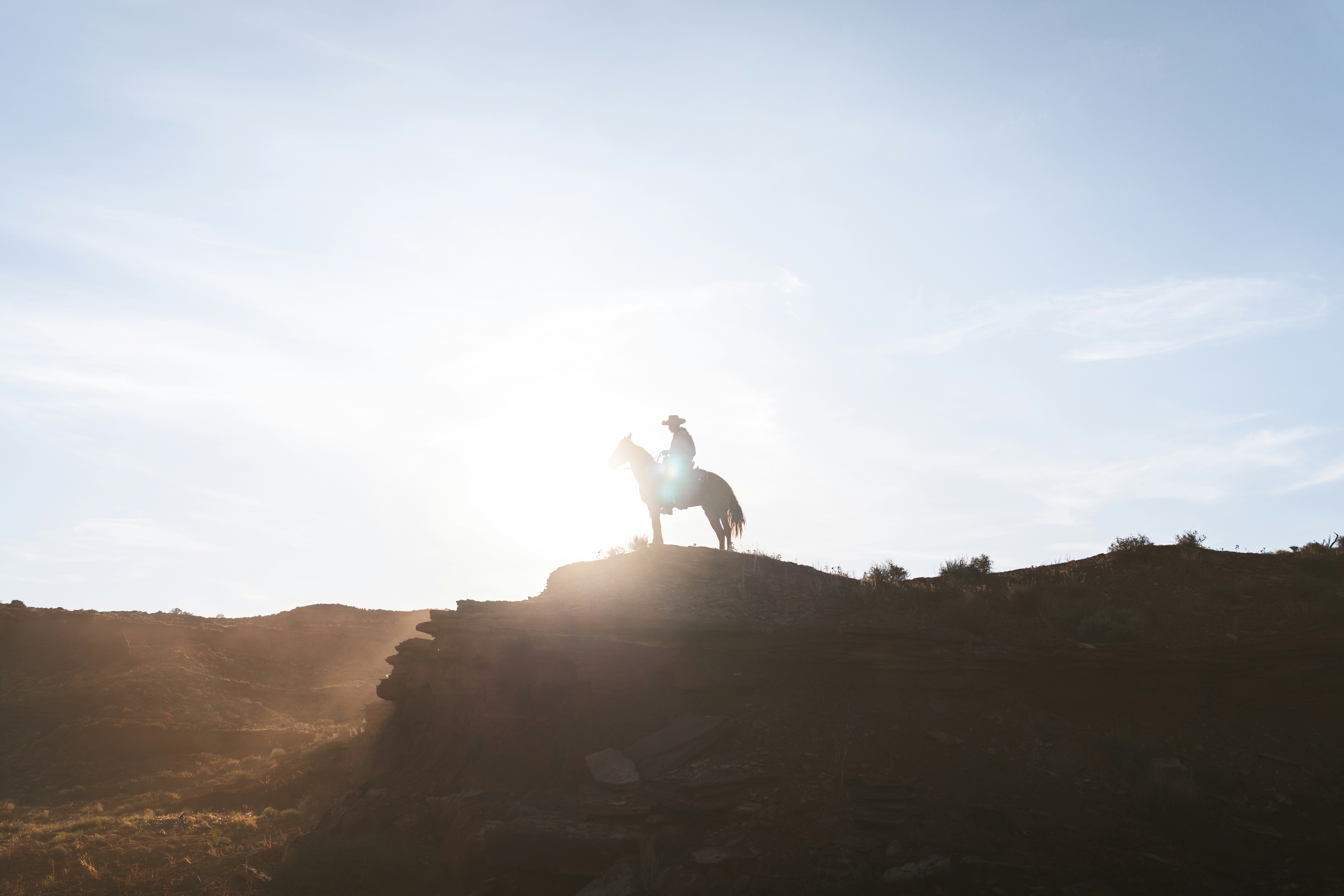 Cowboy a cavallo su una collina al tramonto.