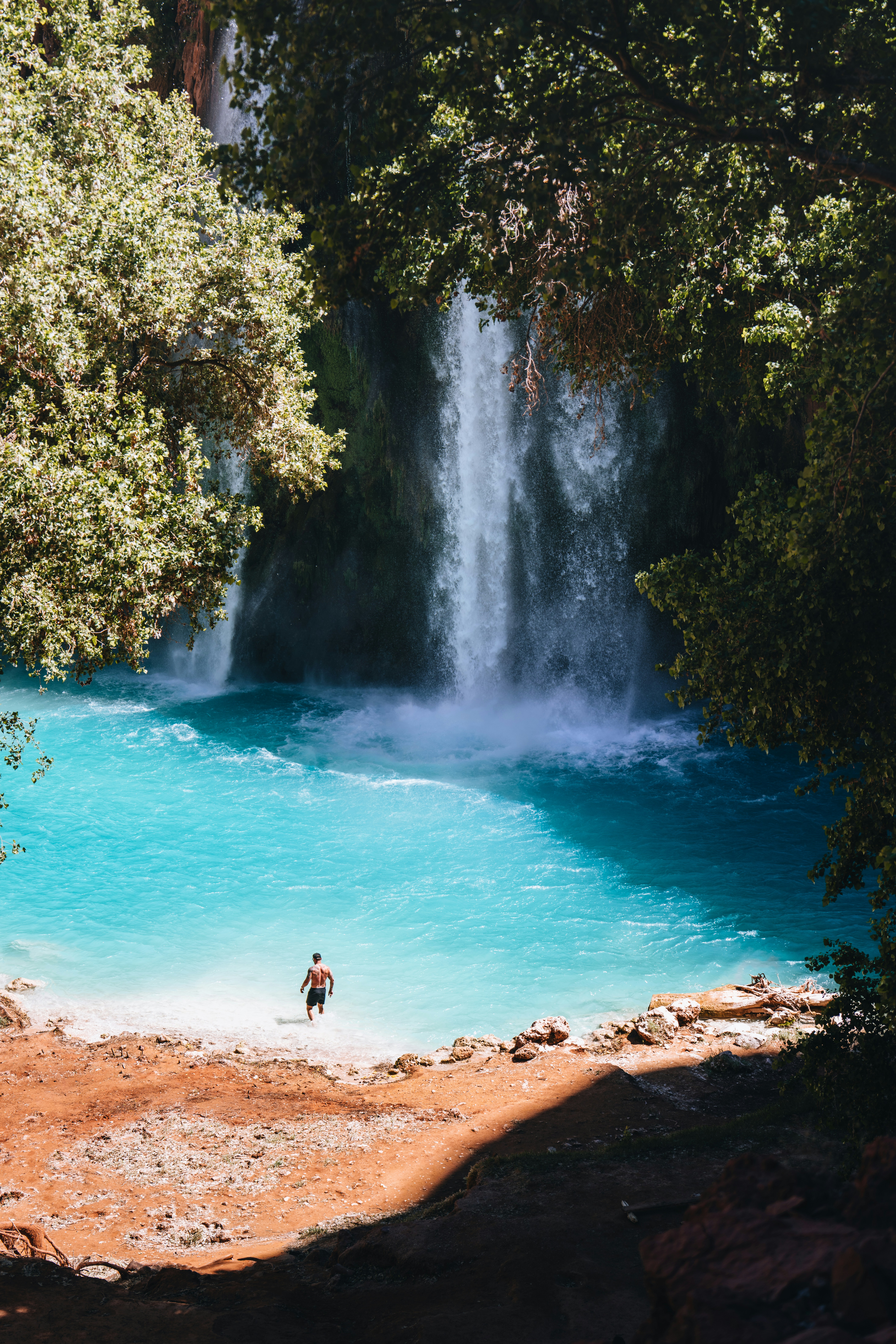 Man standing in turquoise water near a waterfall