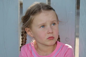 A young girl with braided hair looks thoughtfully aside.