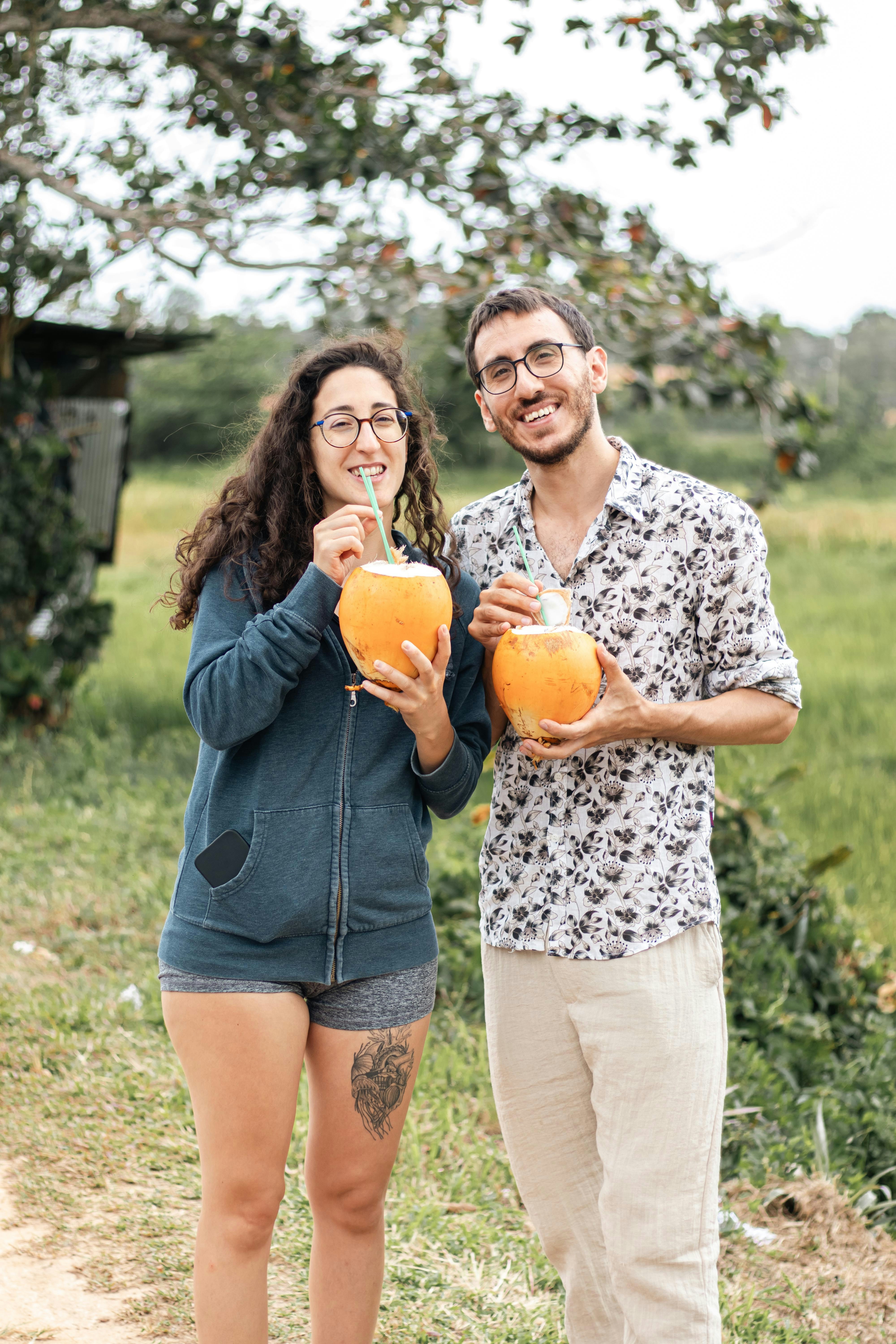 A man and woman smiling while drinking fresh coconuts outdoors.