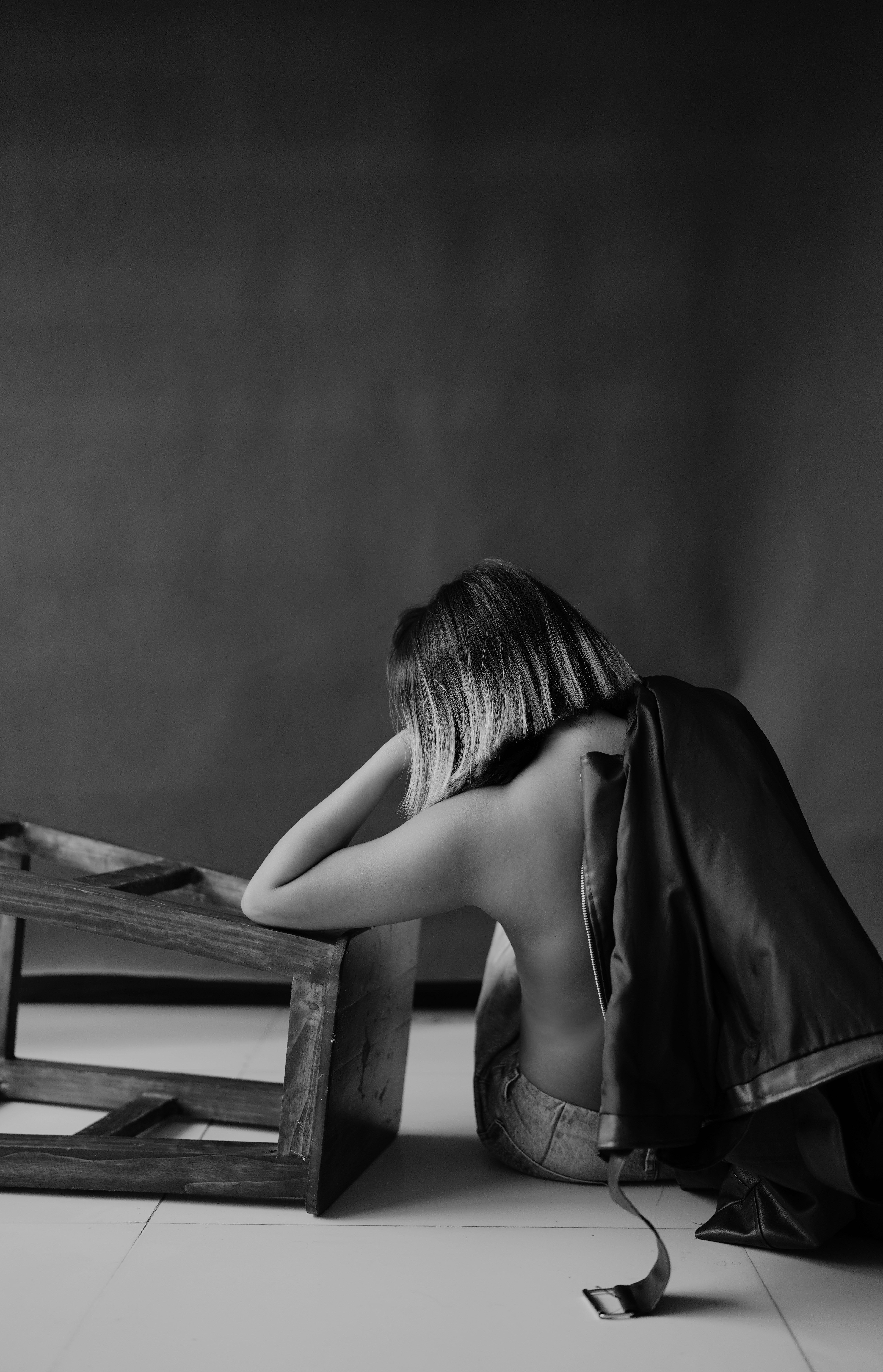 Woman in jacket resting head on arms near wooden stool.