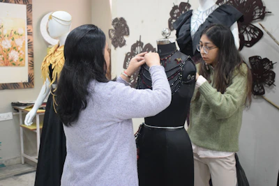 Two women adjusting a black dress on a mannequin.
