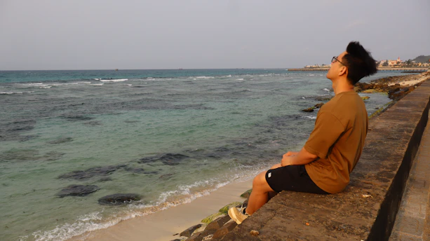 Man sitting by the ocean looking upwards