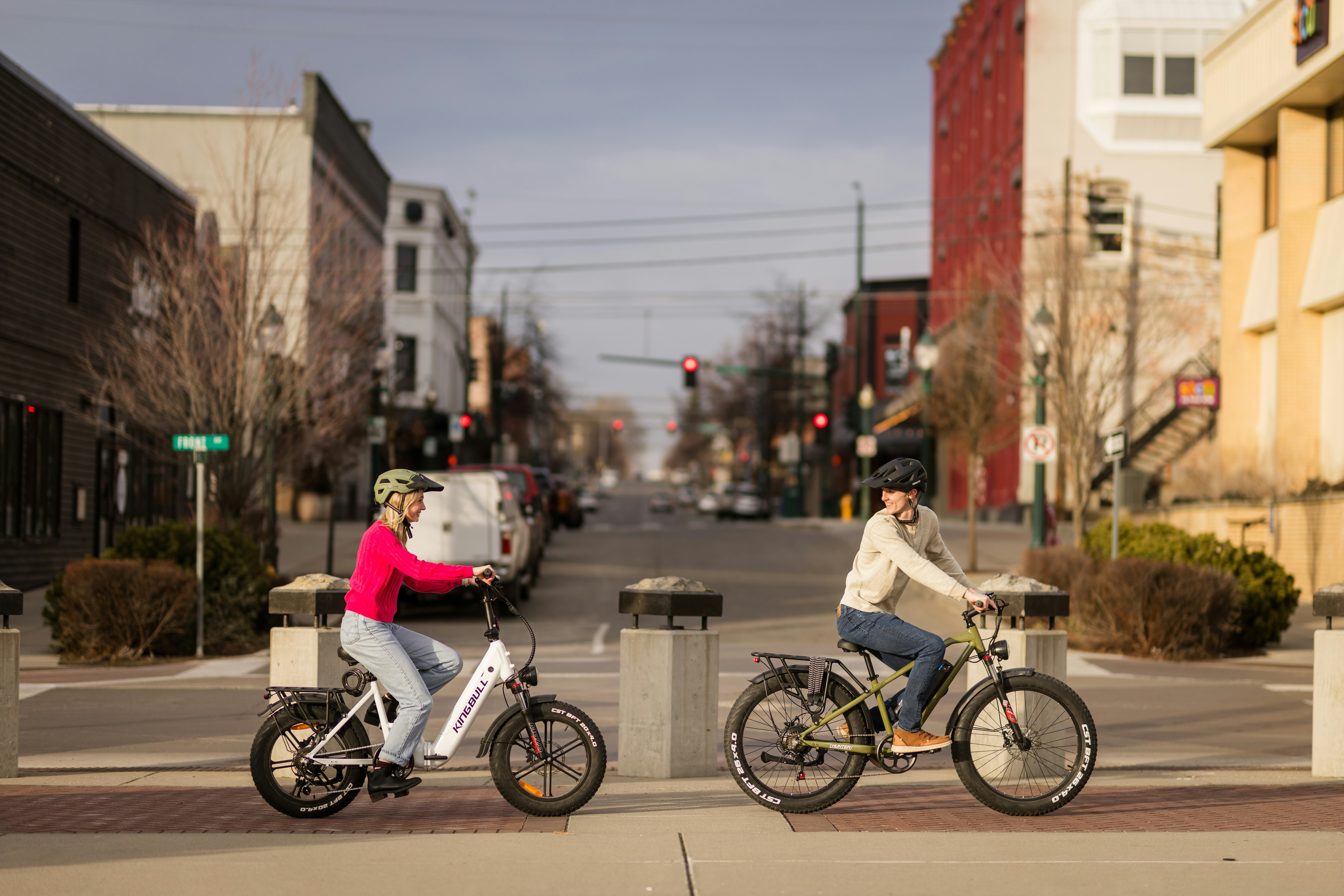 Two people riding electric bikes down a street.
