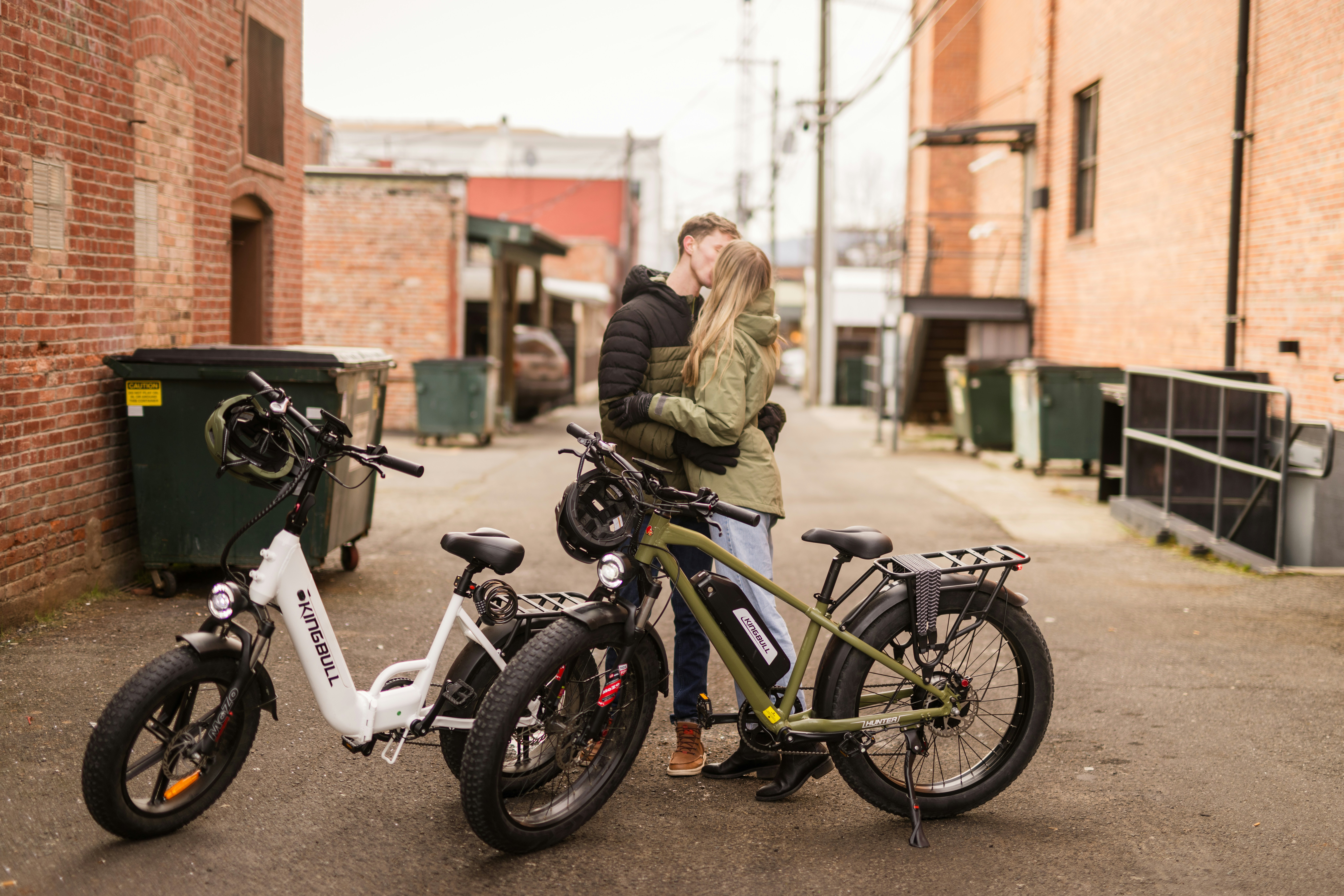 Casal se beijando entre duas bicicletas elétricas em beco