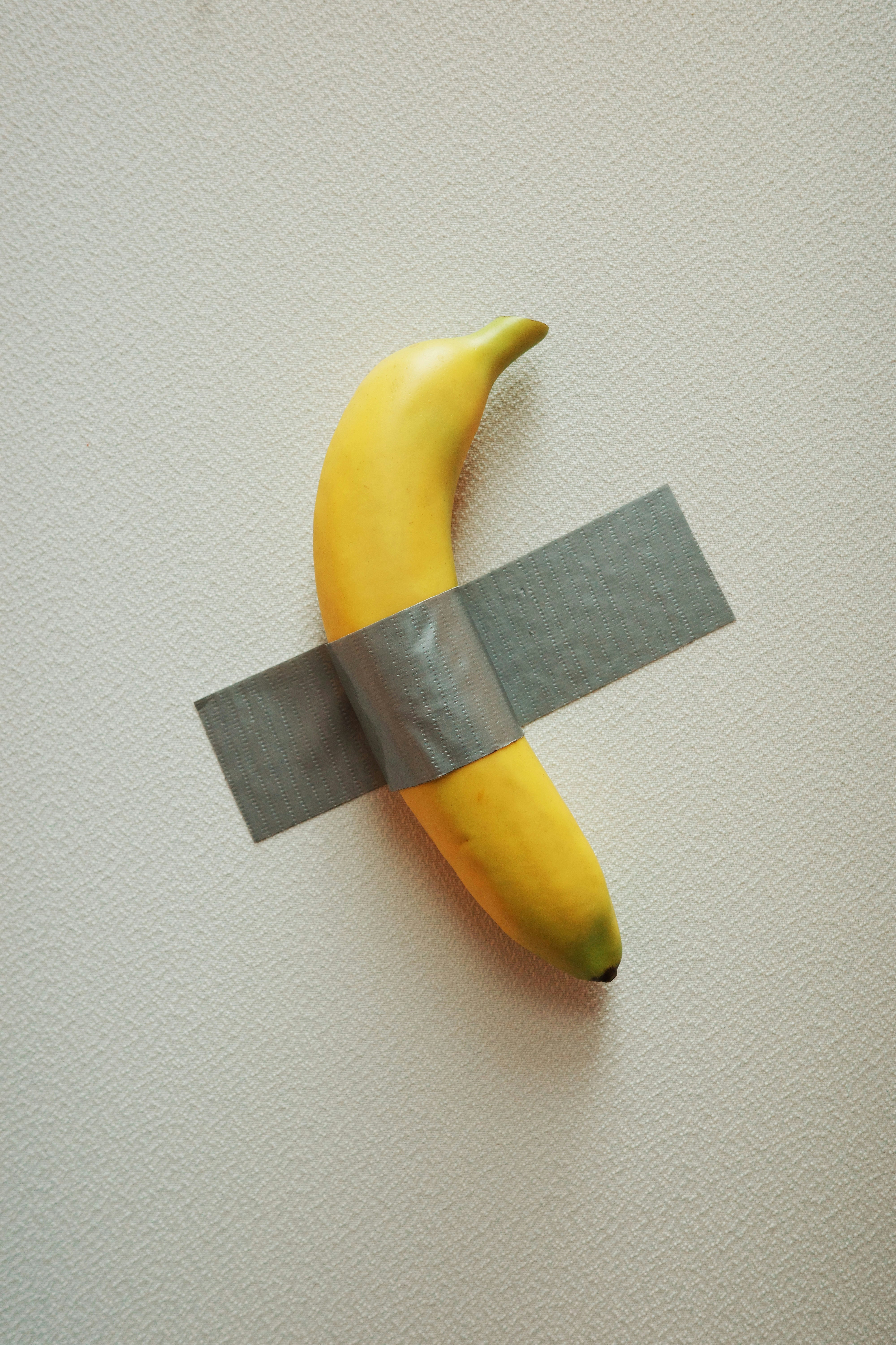 A single banana taped to a white wall.