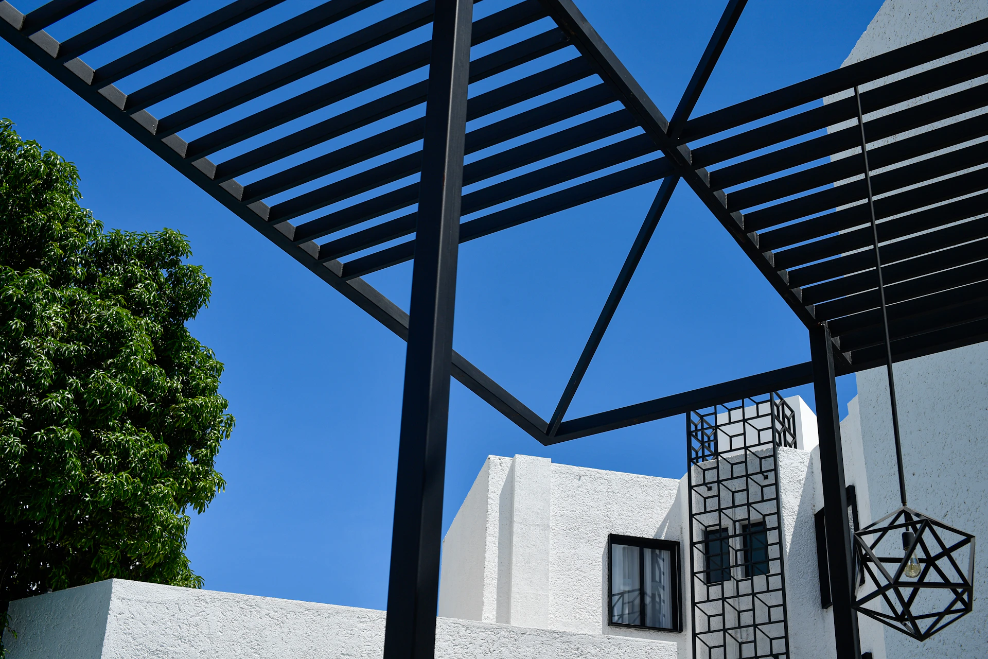 Modern black pergola structure against a clear blue sky.