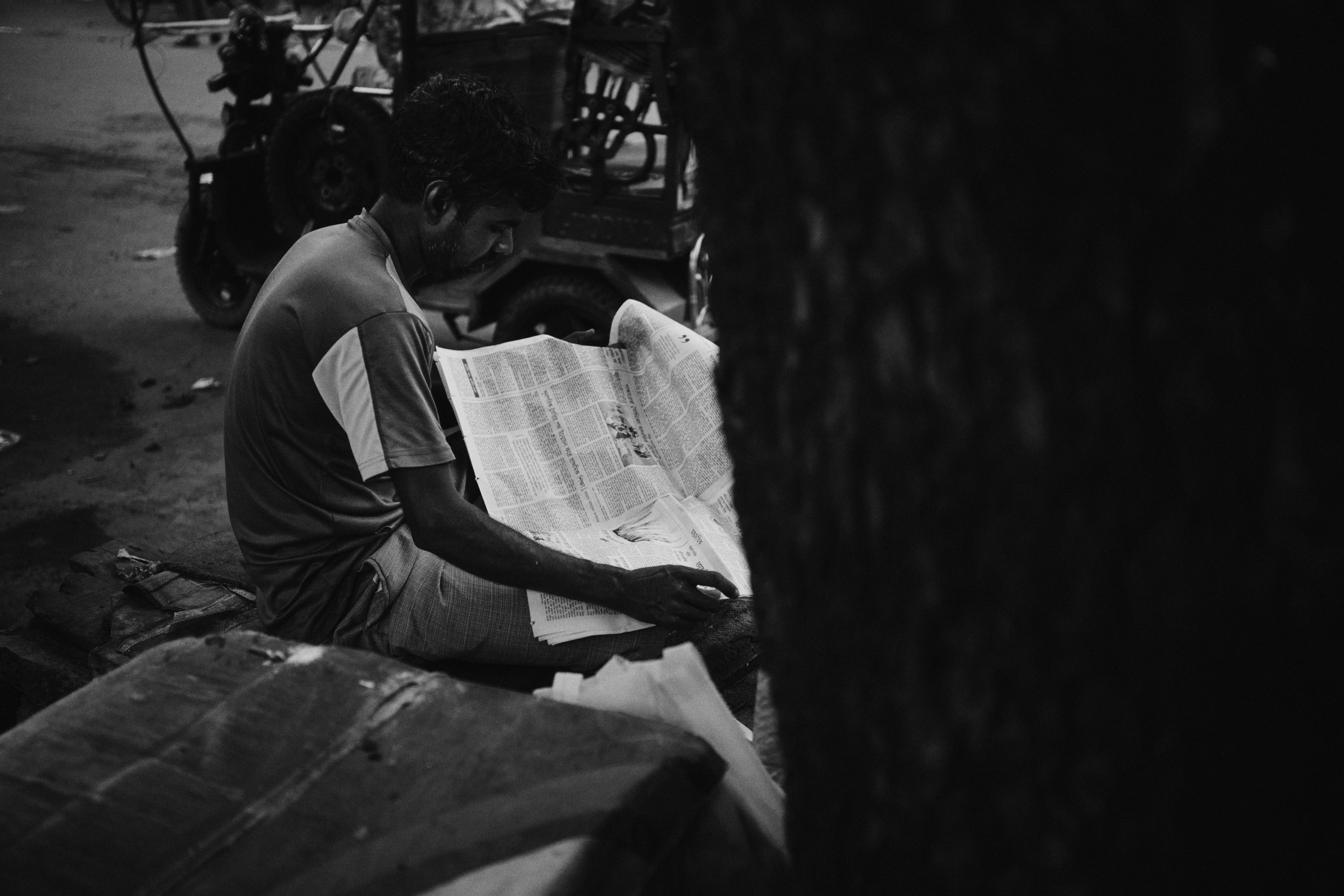 Man sitting and reading a newspaper outdoors.