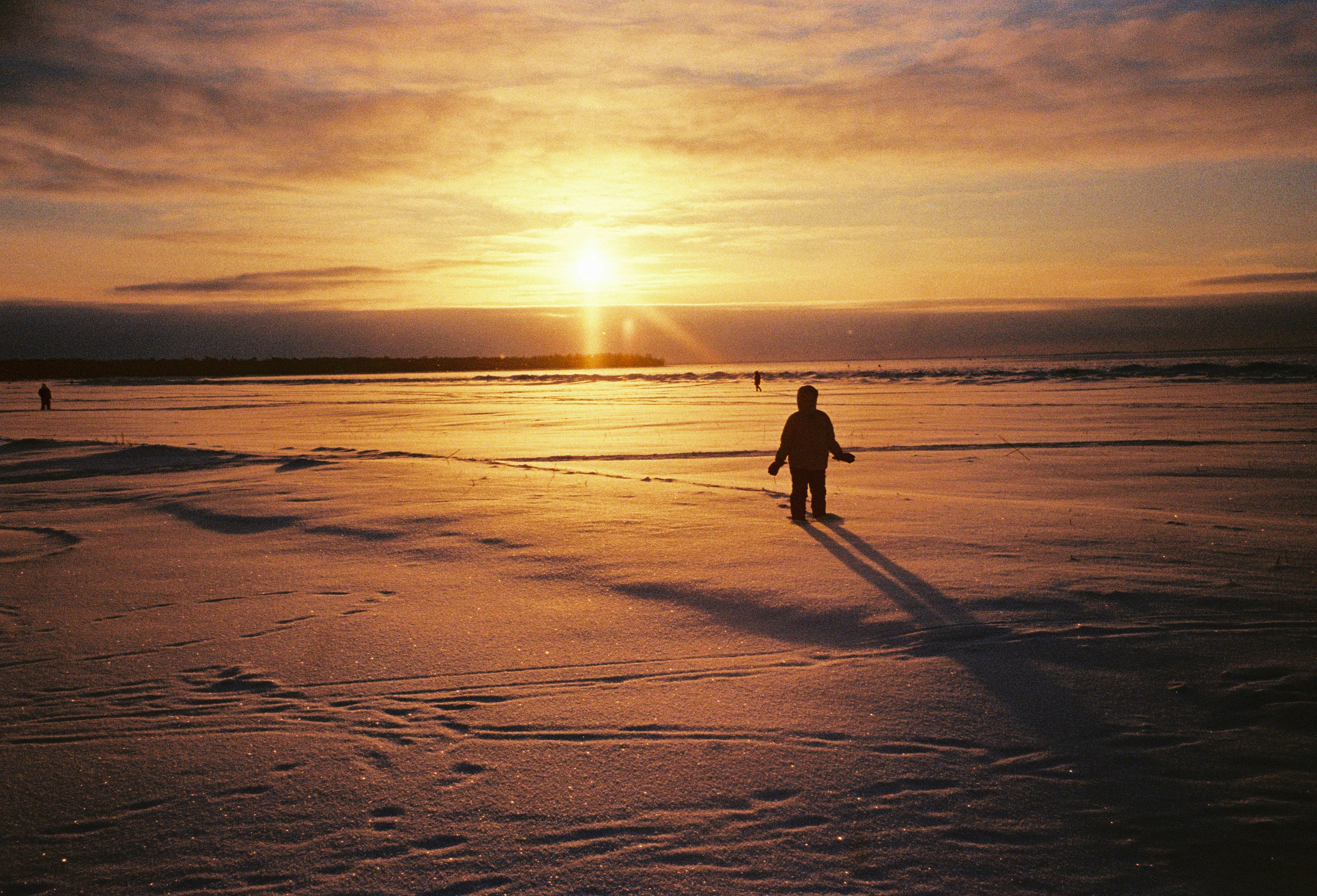 Child silhouetted against a bright sunset on a snowy field.