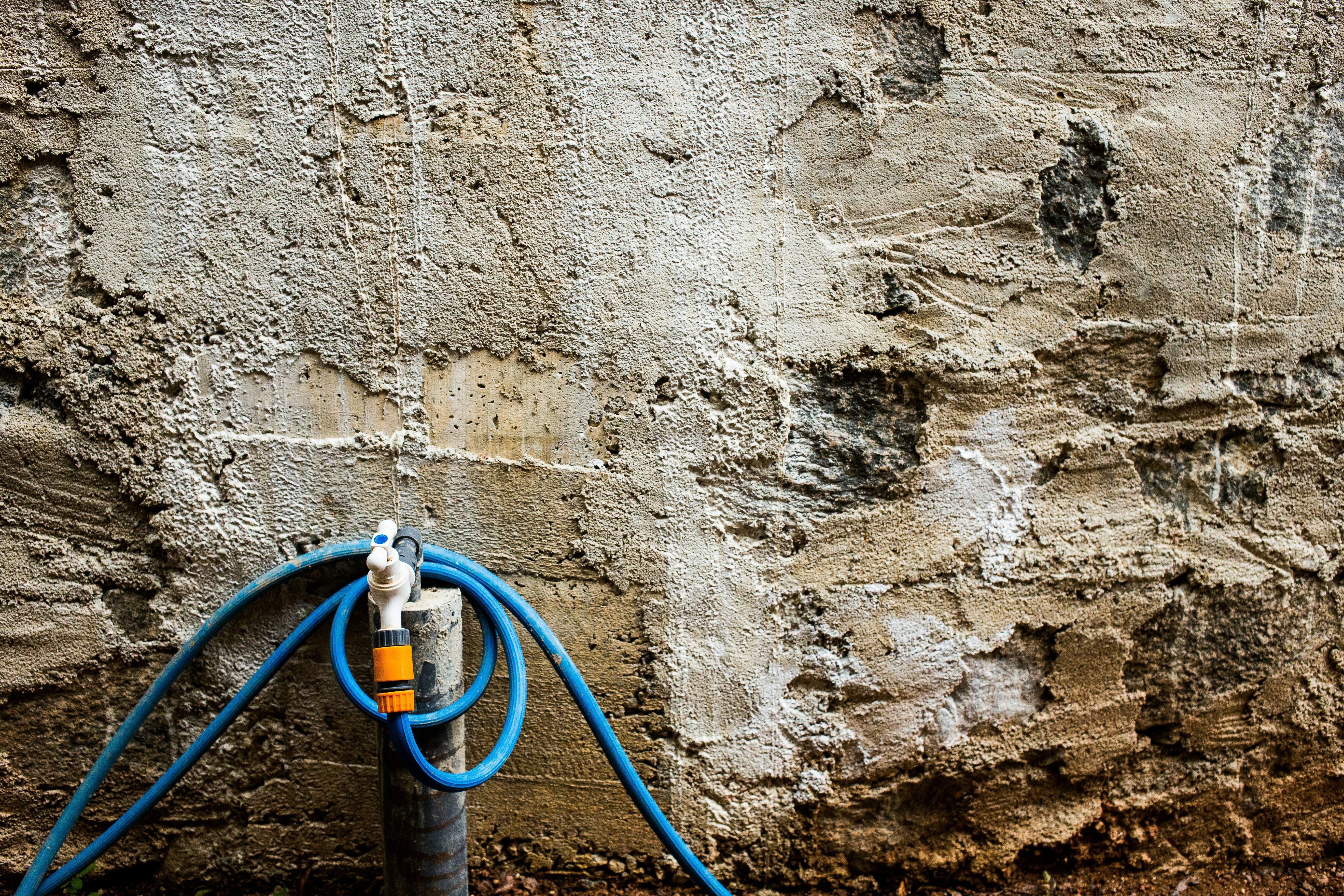 Blue hose coiled around a spigot against a textured wall.