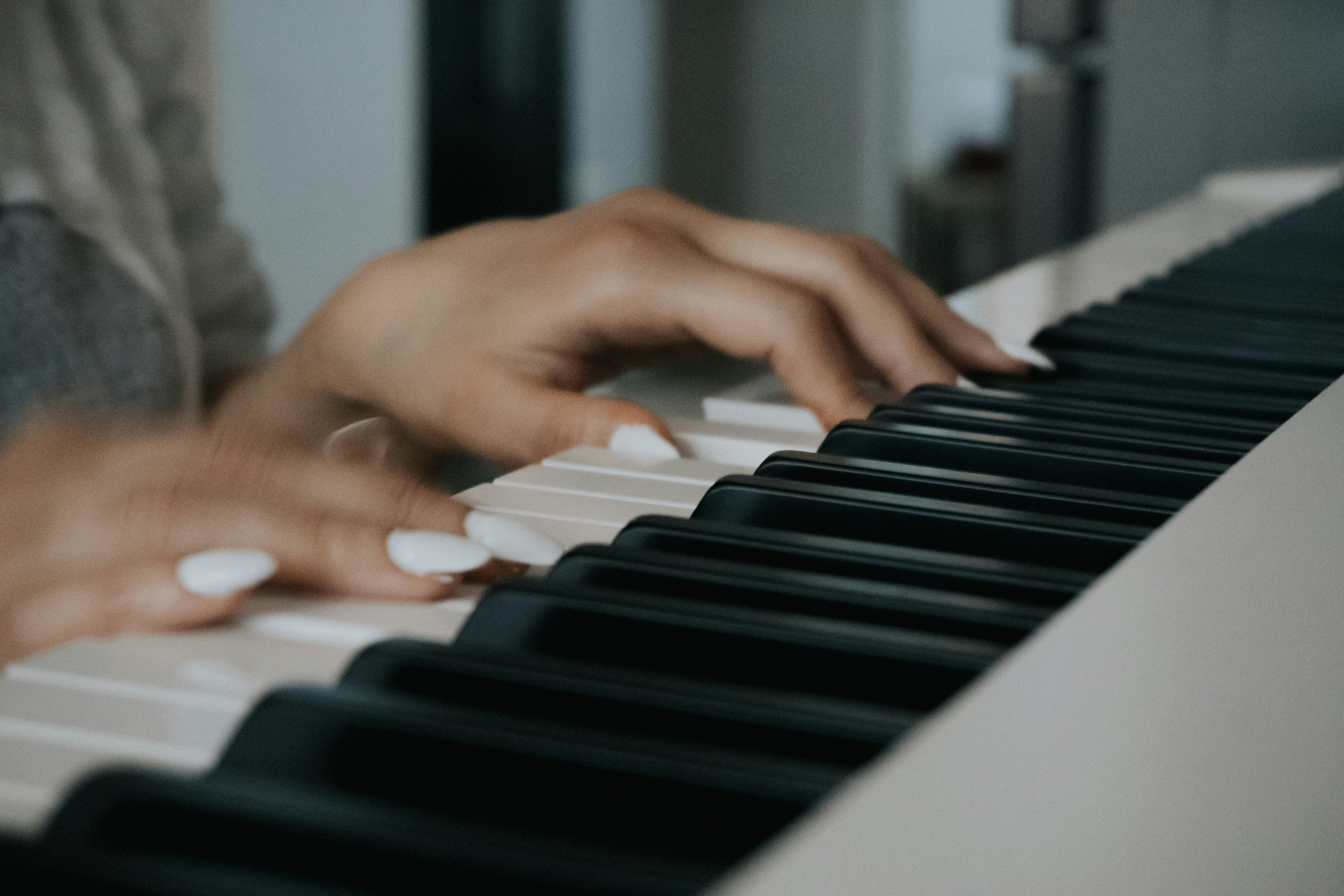 Hands with white nails playing a piano keyboard.