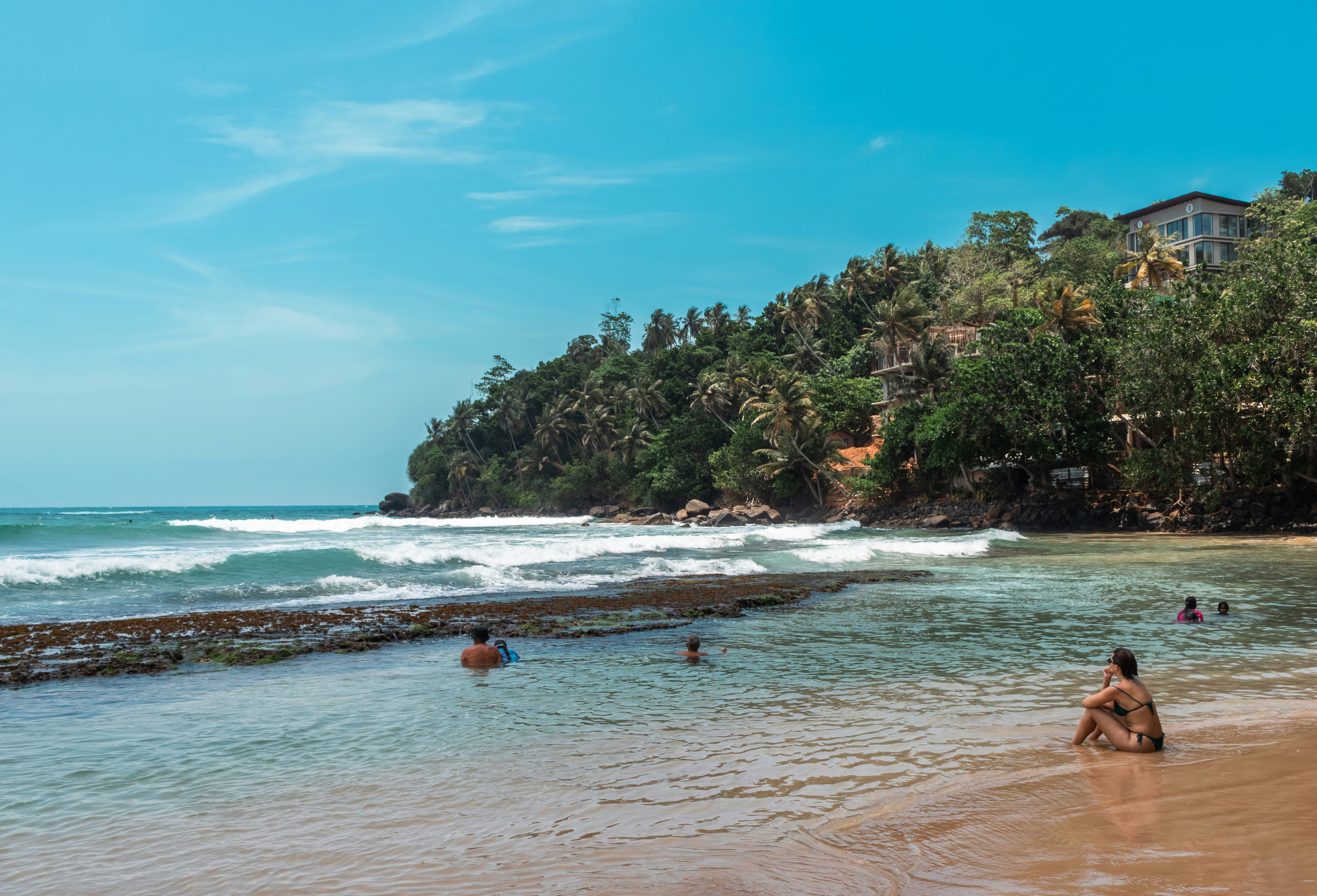 Tropical beach with swimmers, gentle waves, and a green hillside.