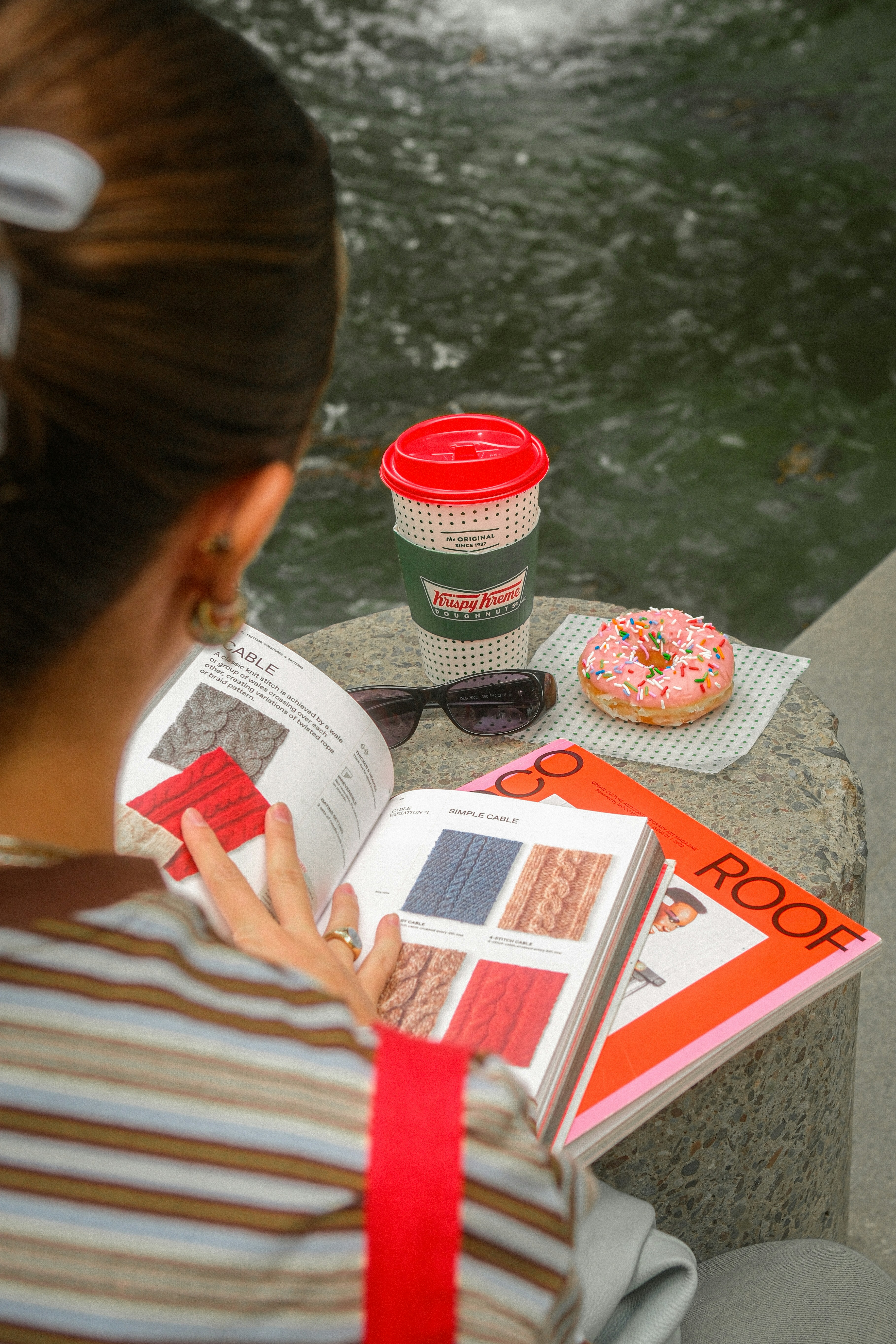 Woman reading a book beside coffee and a pink donut