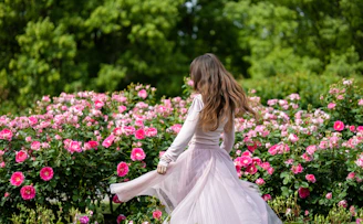 Woman in a flowing dress among blooming pink roses.