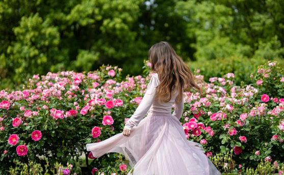 Woman in a flowing dress among blooming pink roses.