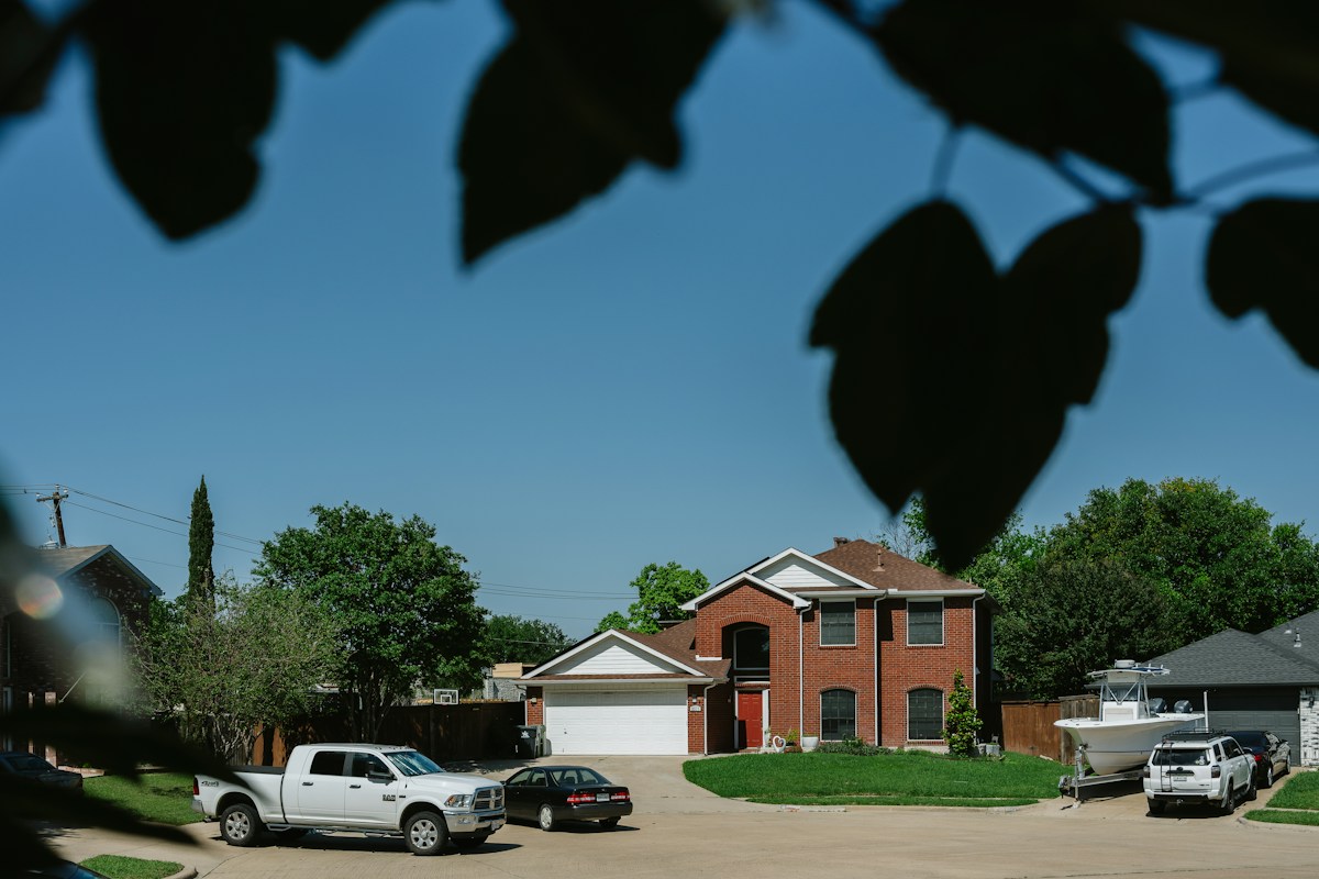Two cars parked in a driveway of a brick house, ready for a youth sports carpool.